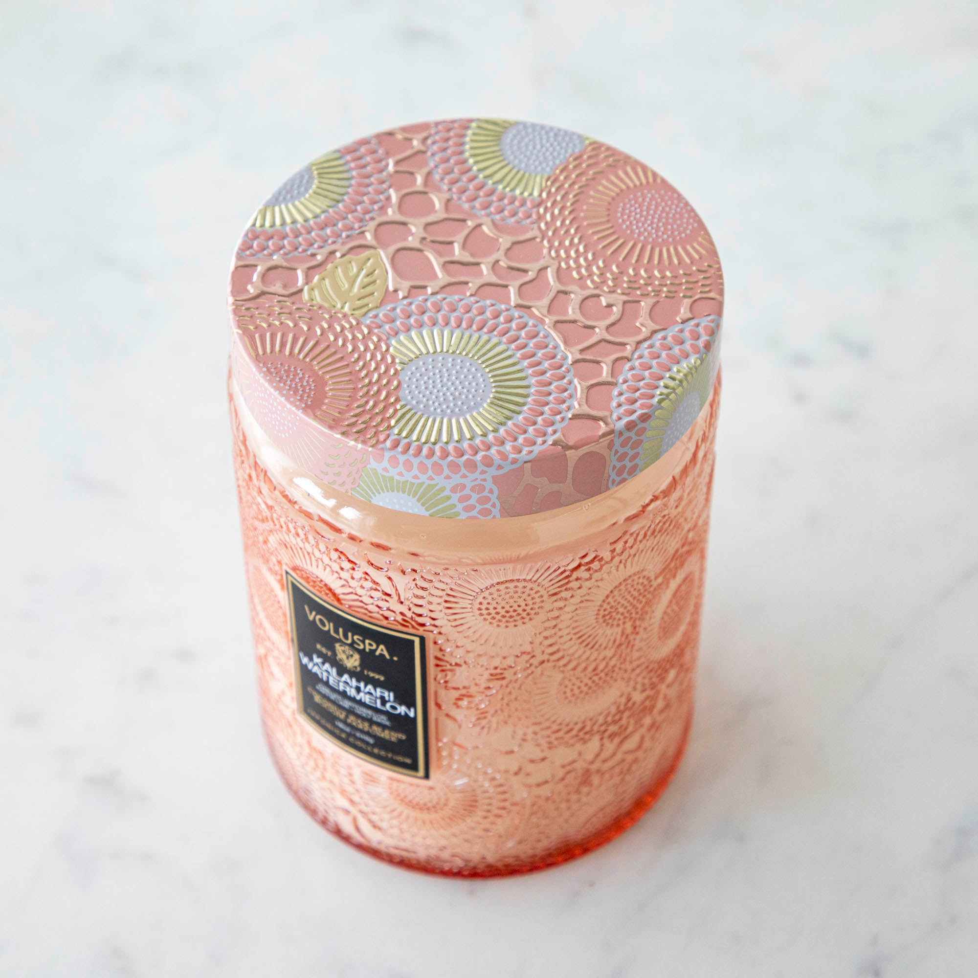 Two Voluspa Kalahari Watermelon candles on a marble surface with matches nearby, featuring a crisp cucumber aroma.