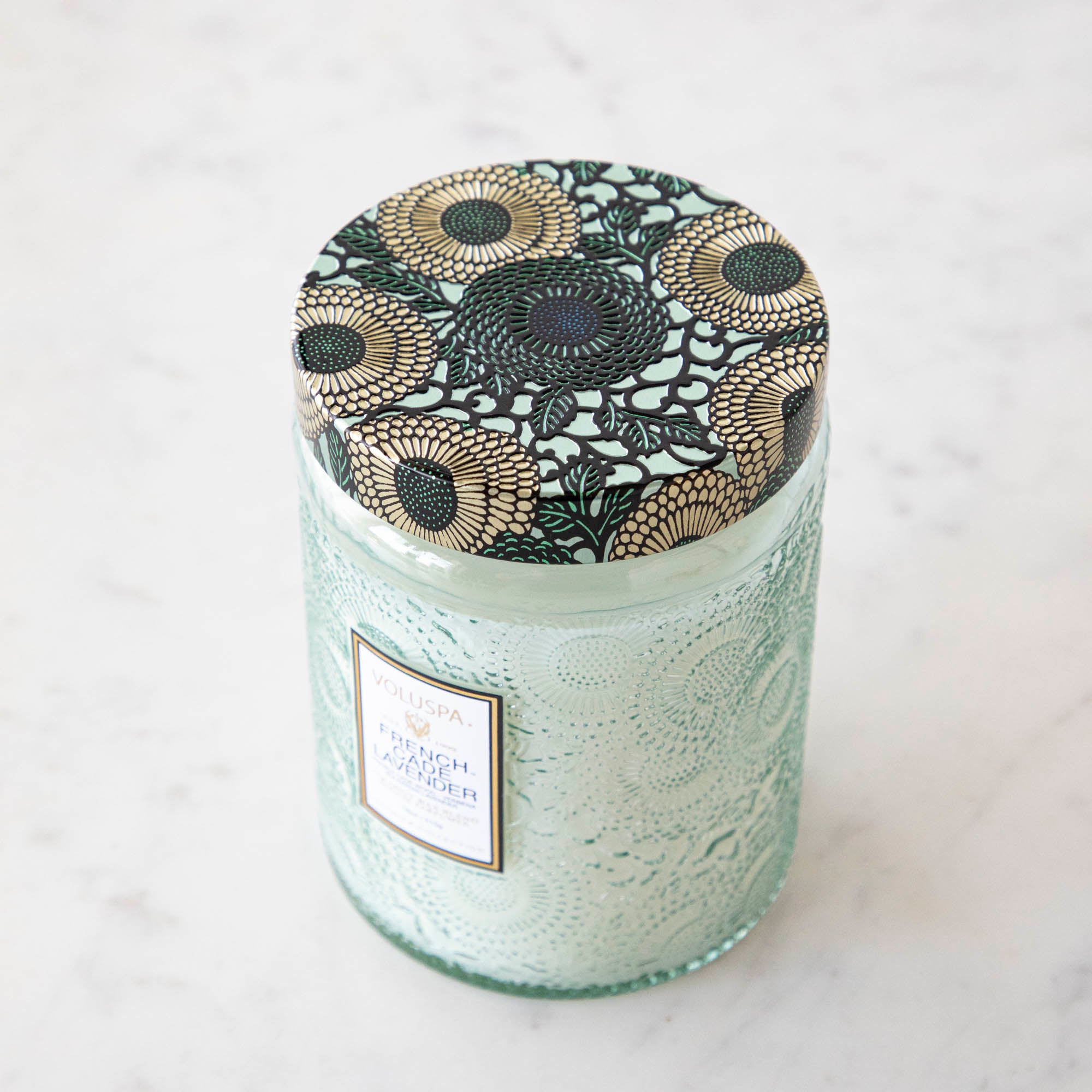 The Voluspa French Cade Lavender 18oz candle lid with a flowered detailing in the glass.