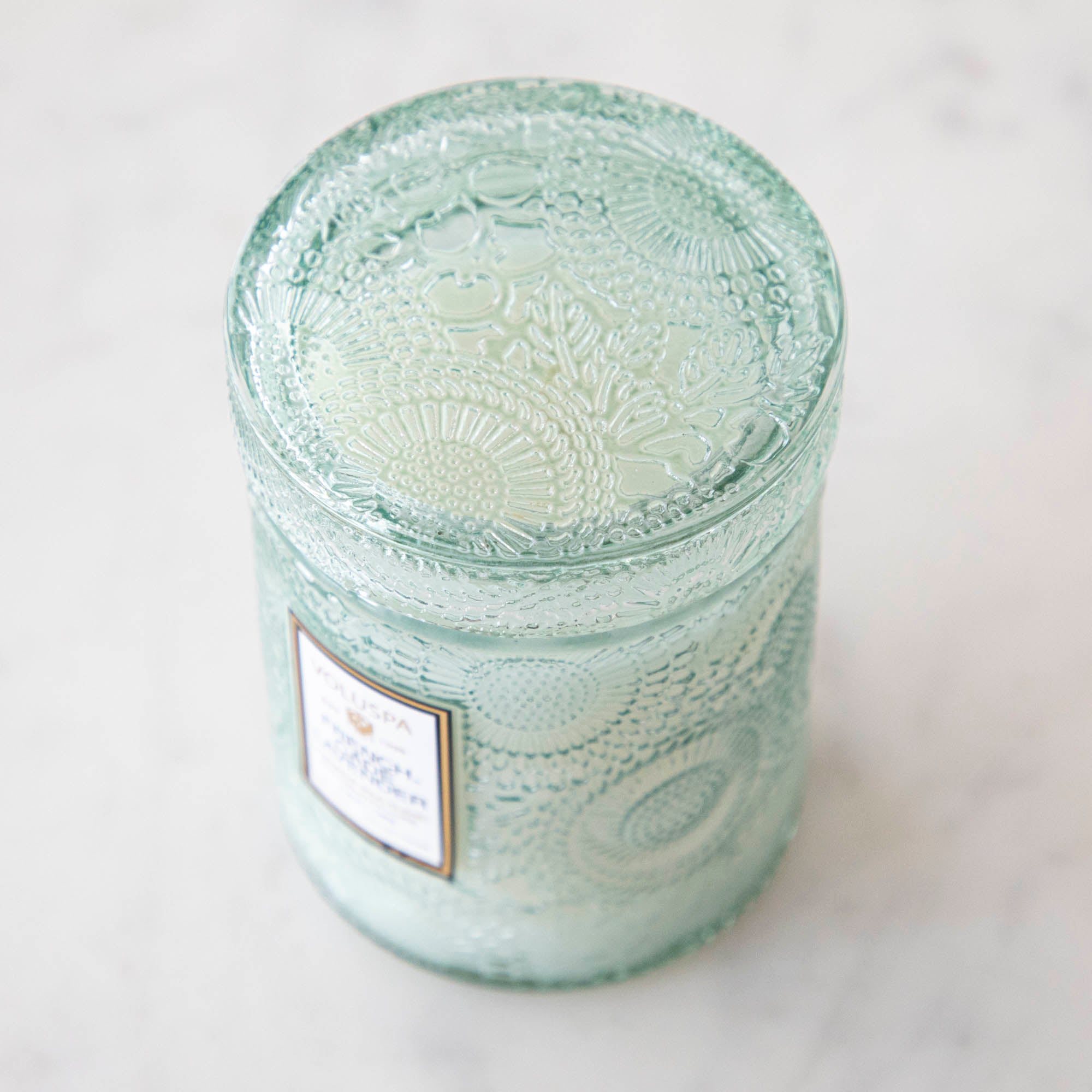The Voluspa French Cade Lavender 5.5oz candle lid with a flowered detailing in the glass.