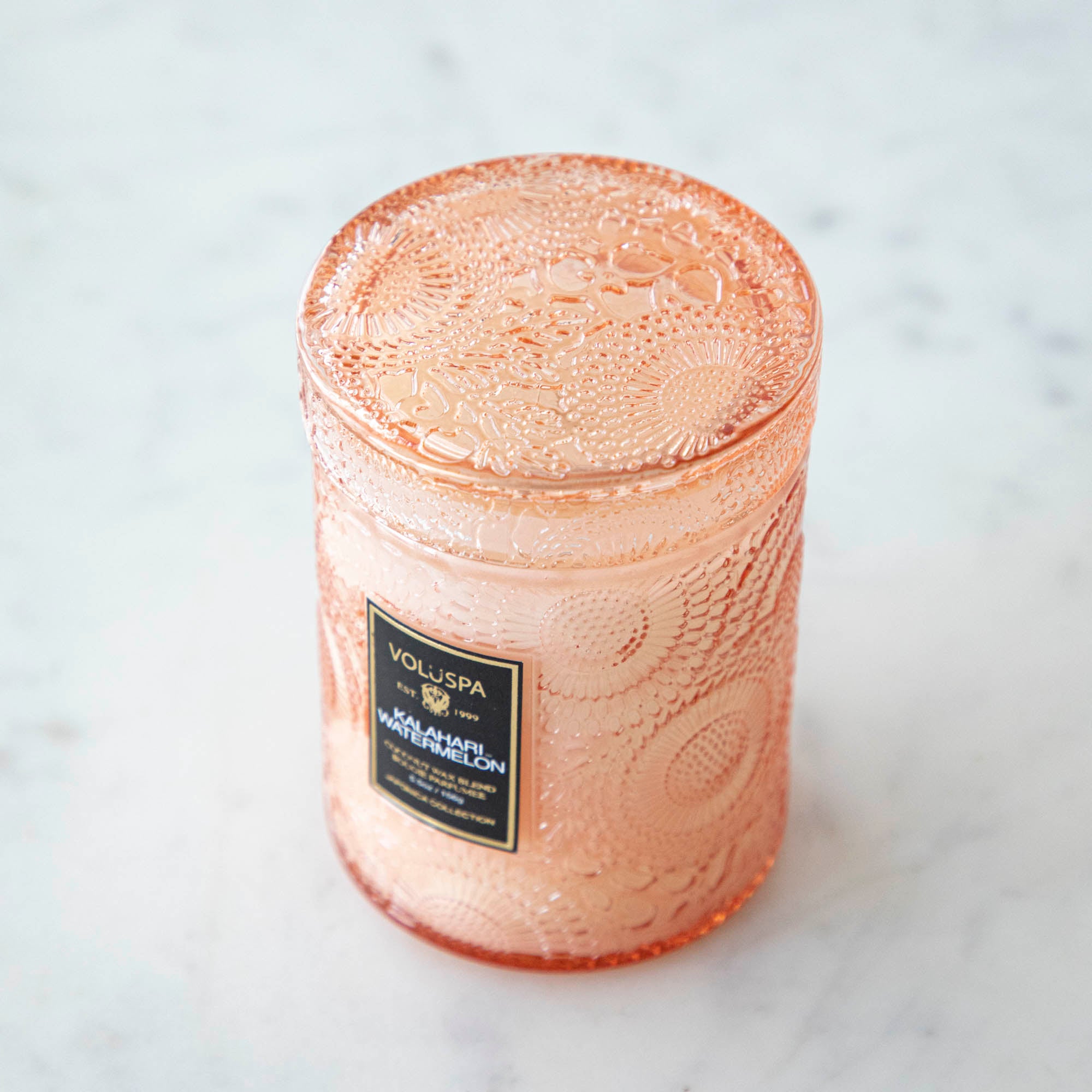 Two Voluspa Kalahari Watermelon candles on a marble surface with matches nearby, featuring a crisp cucumber aroma.