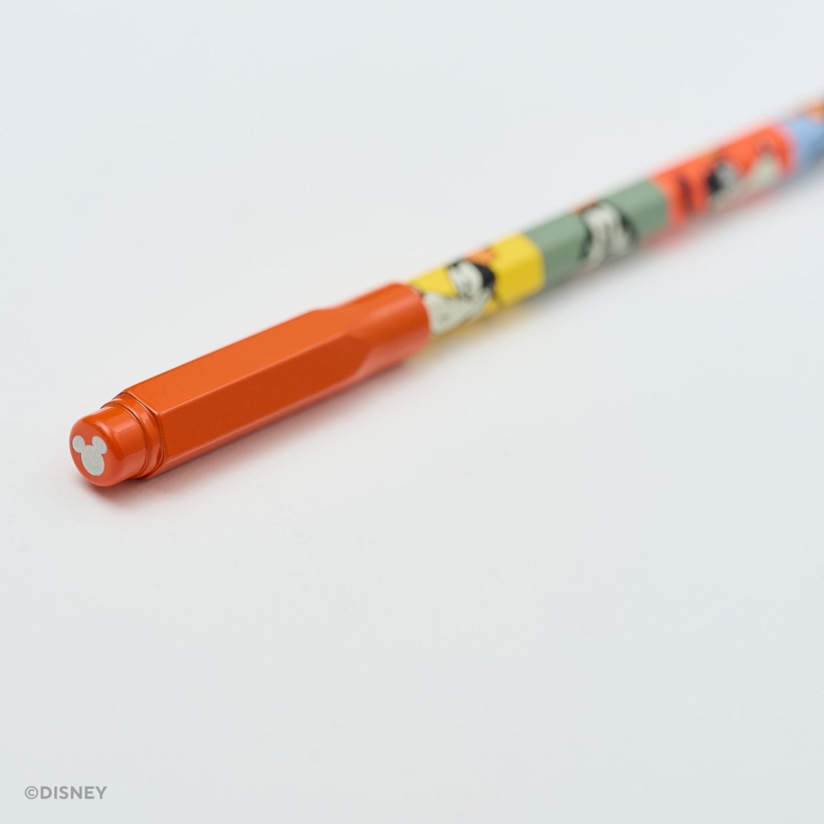 A close-up of a Disney pencil with a bright orange point guard and a multicolor body featuring cartoon character illustrations, photographed on a clean white background.