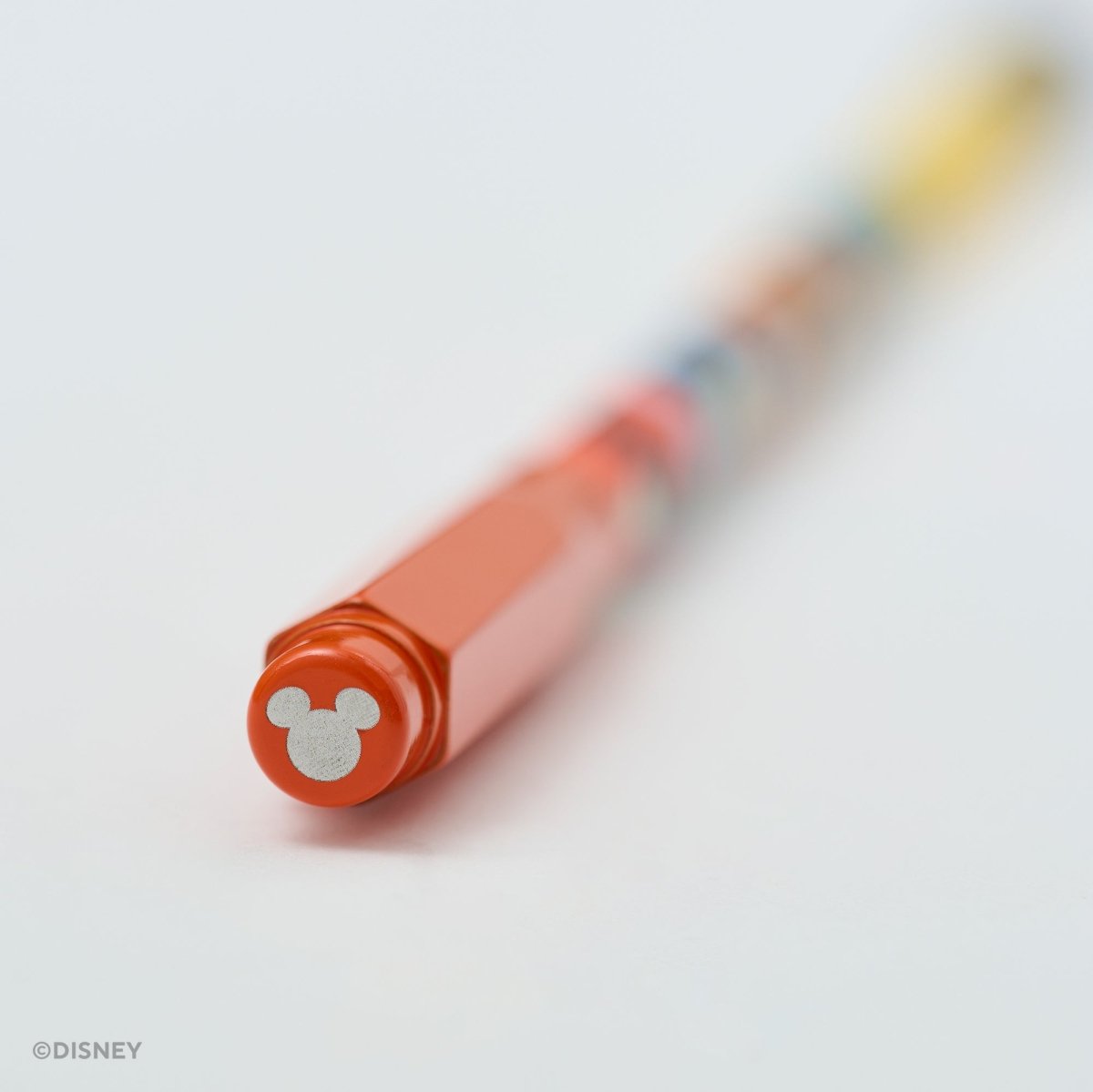 A close-up of a Disney branded orange pencil cap with a silver Mickey Mouse head logo on the cap, shown on a clean white background with a shallow depth of field.