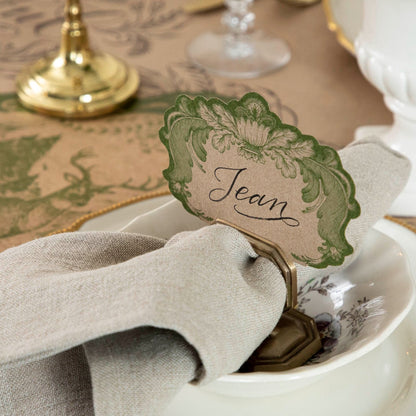 A Moss Fable Toile Place Card labeled &quot;Jean&quot; standing in a napkin ring place card holder, as part of an elegant table setting.