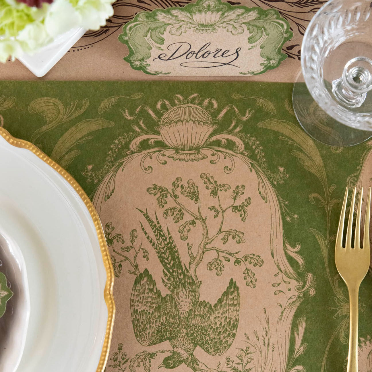 Close-up of the Moss Fable Toile Placemat under a place setting, showing the peasant illustration in detail.