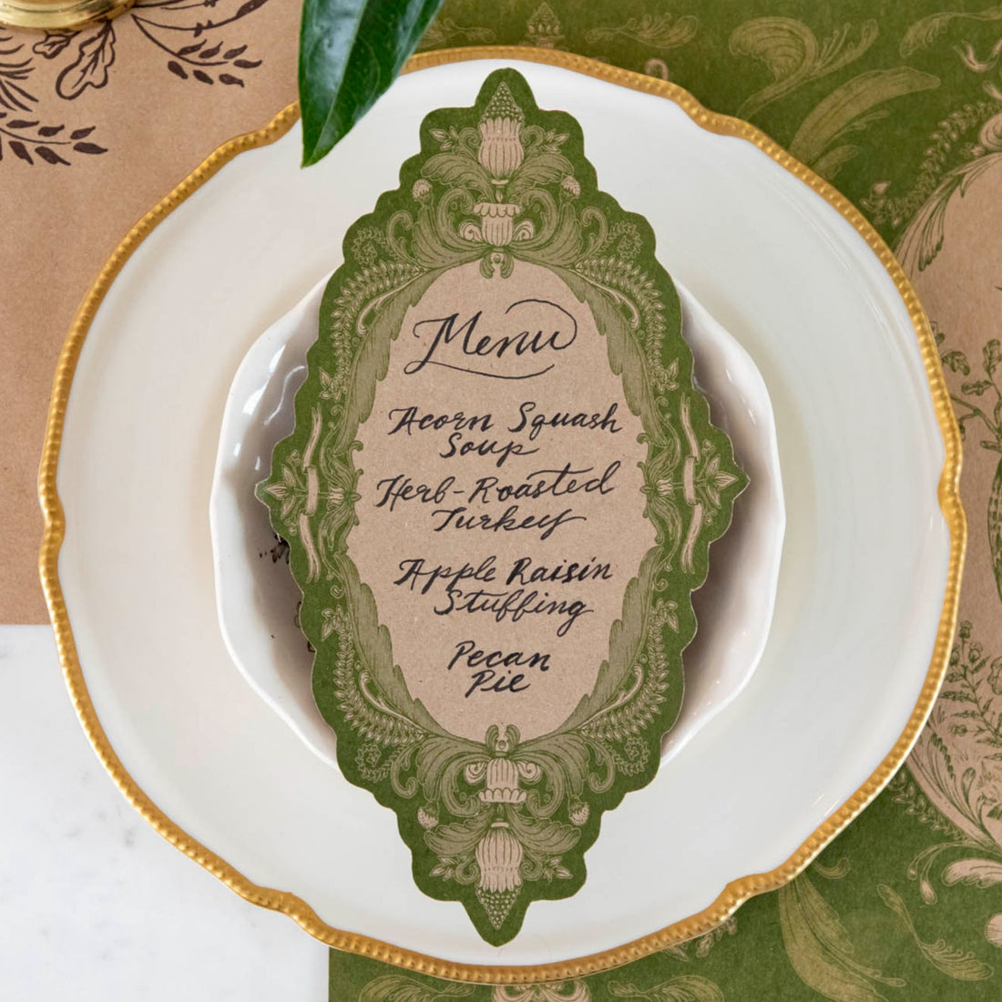 A Moss Fable Toile Table Card with a menu written on it in beautiful script resting on the plate of a rustic place setting.