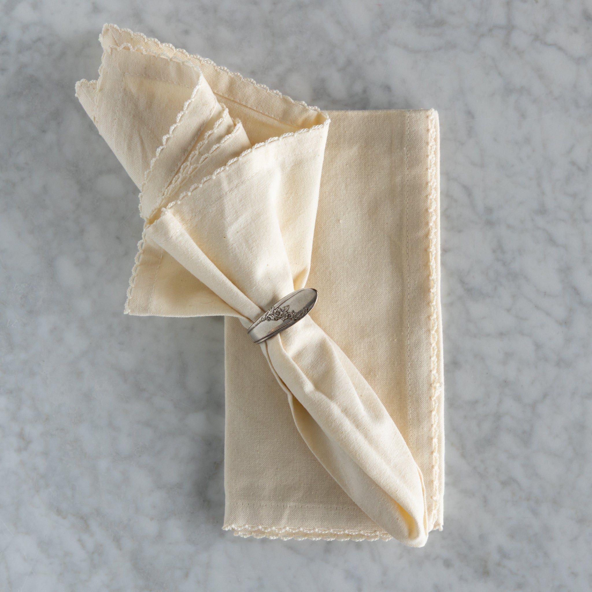 Folded beige napkin with a silver napkin ring on a gray textured surface.