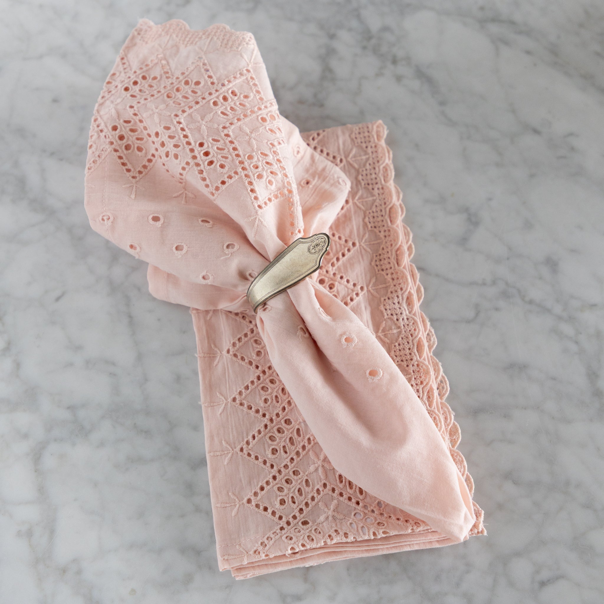 Pink lace napkin with a silver napkin ring on a marble surface.