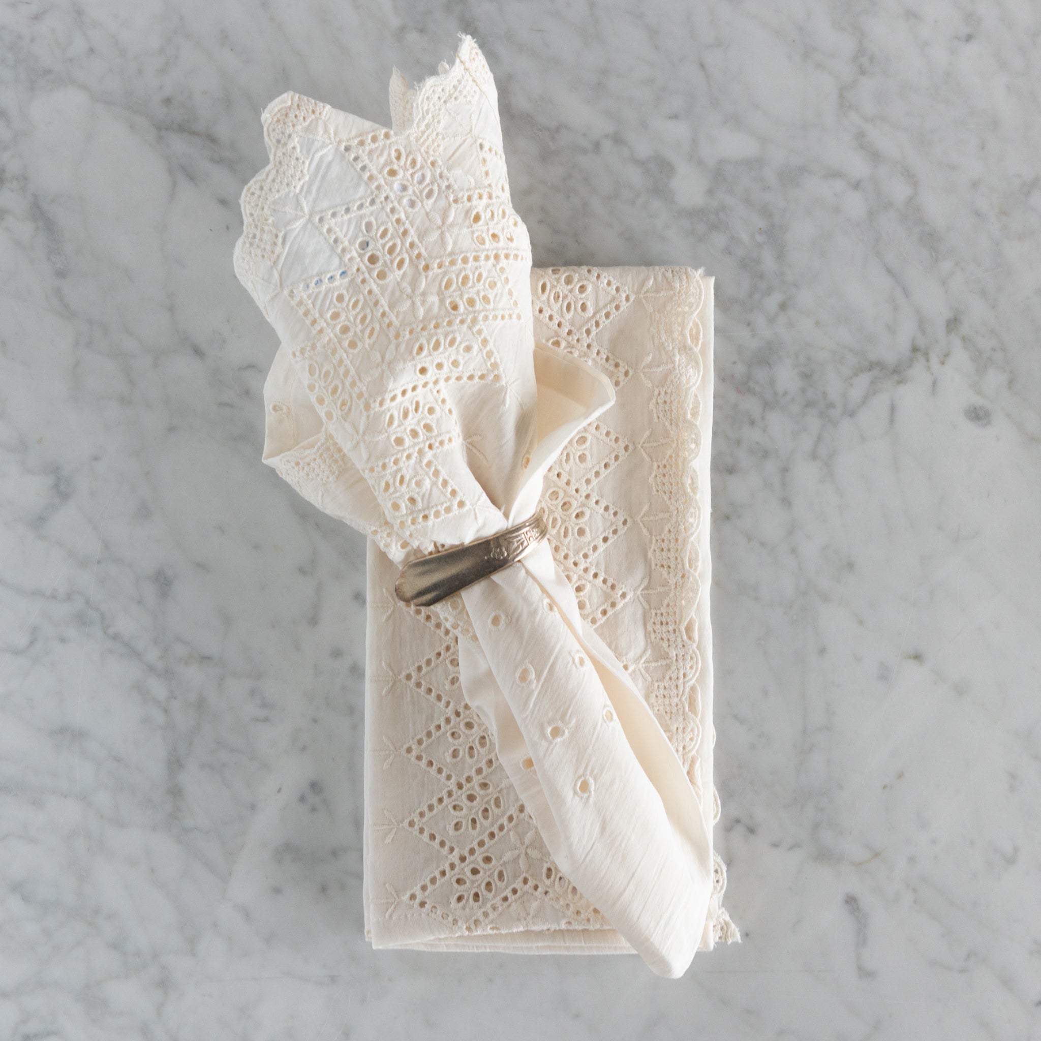 White lace napkin folded and tied with a silver napkin ring on a marble surface.
