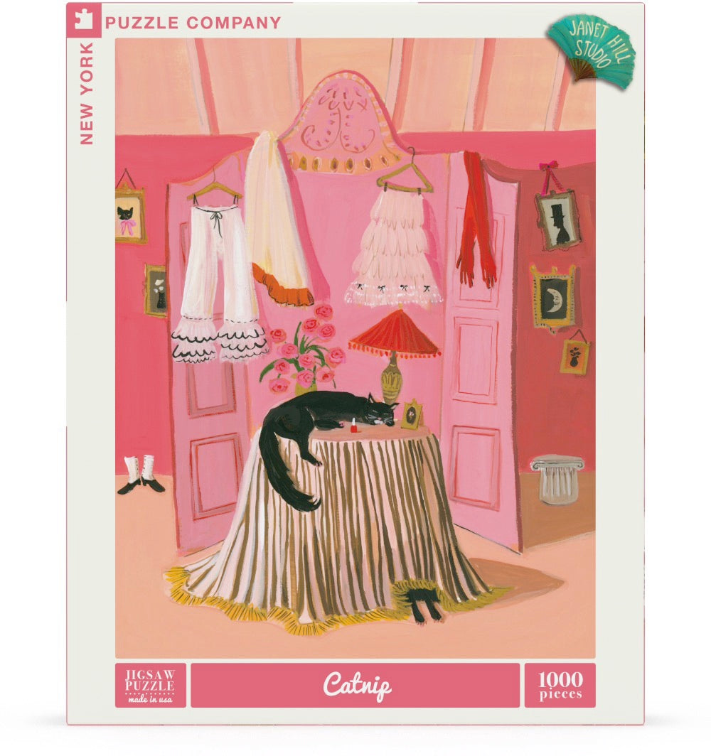 Puzzle box with artwork of a cat sleeping on a round table with a dressing screen behind it in pink with clothes strewn over it. Artwork by Janet Hill.