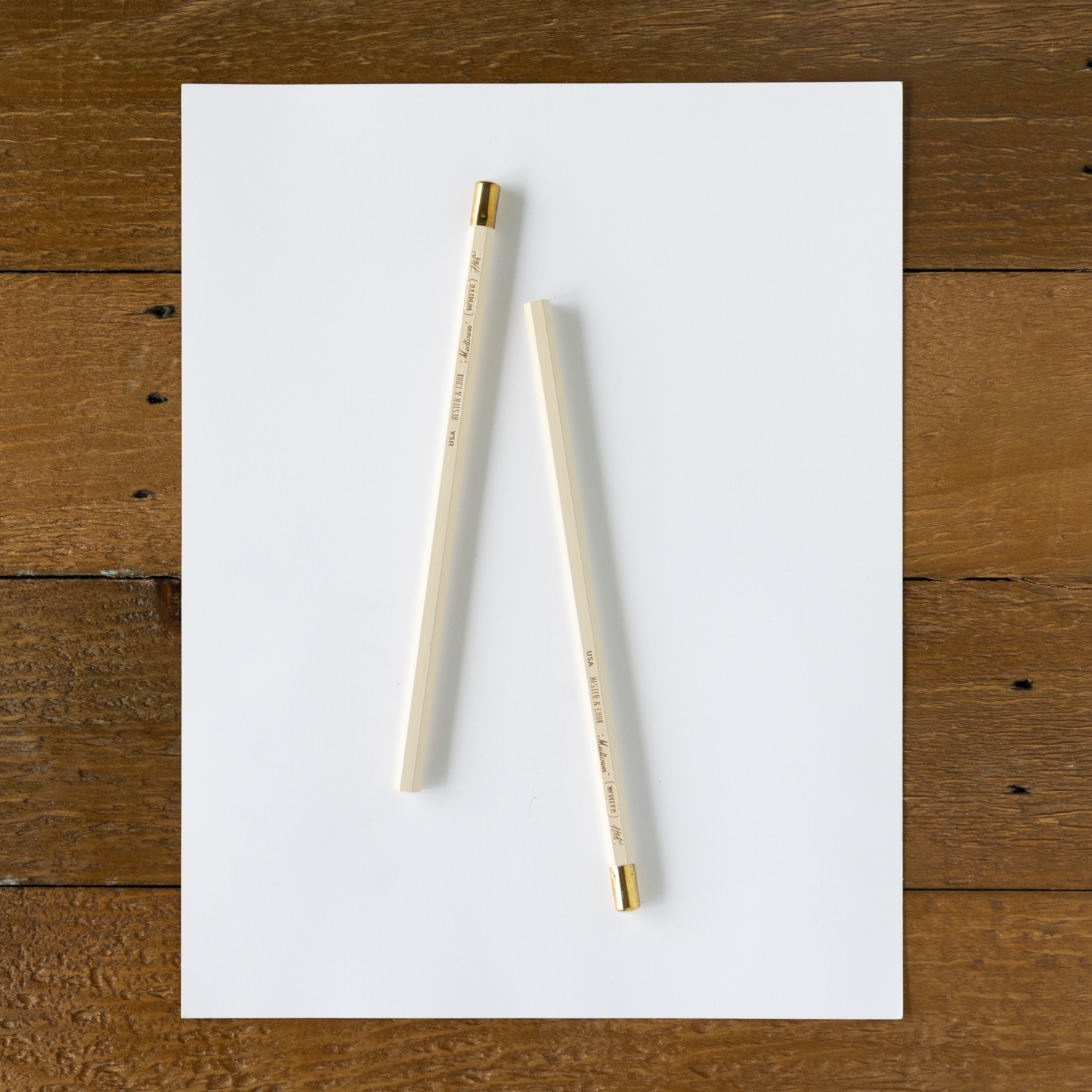 Two pencils on a white sheet of paper with a wooden surface background.
