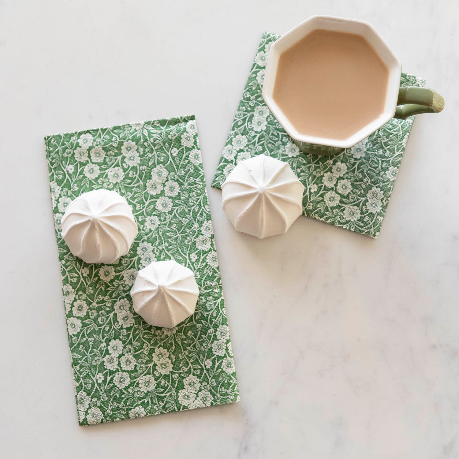 Top-down view of a cup of coffee and marshmallow treats sitting on one Guest and one Cocktail Green Calico Napkin.