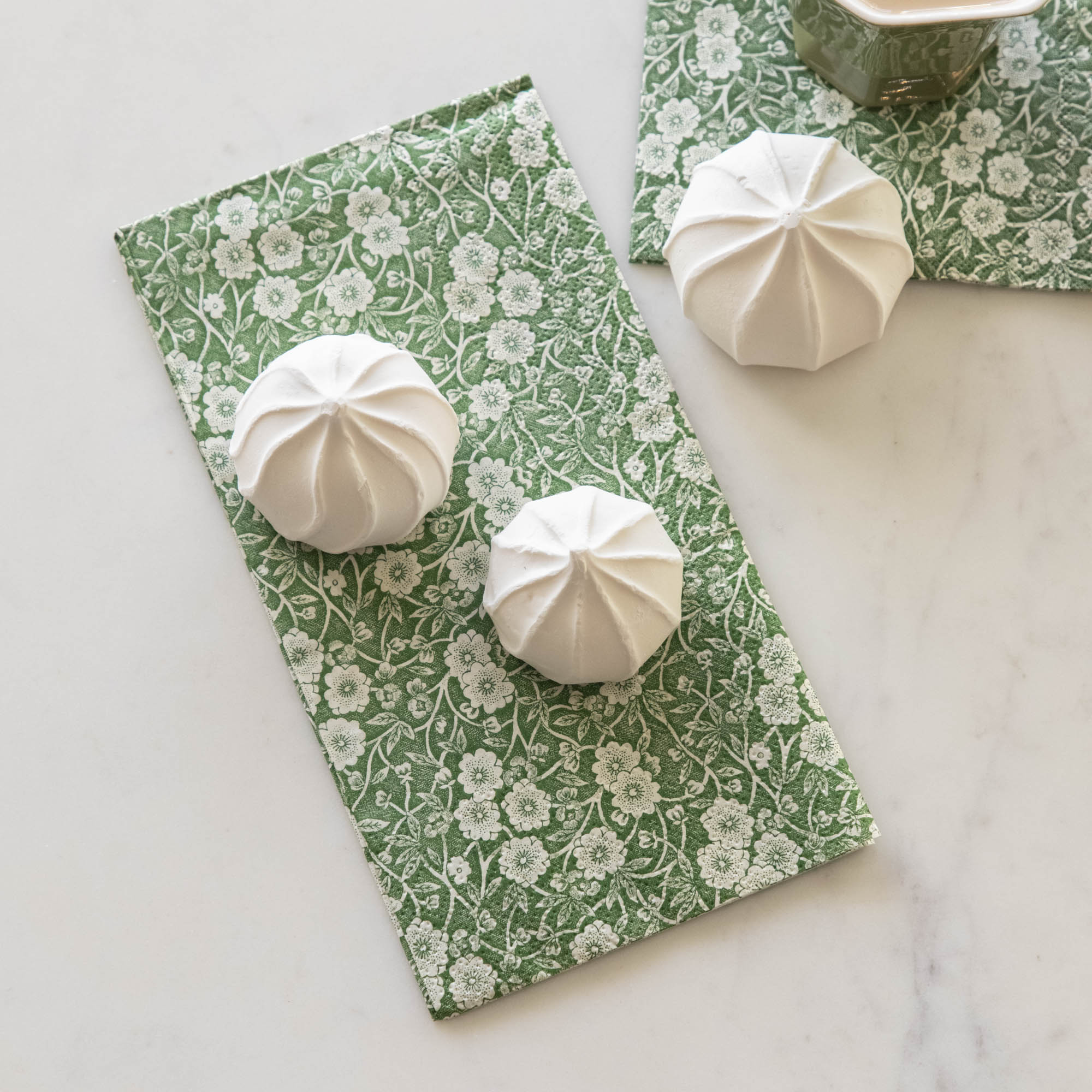 Some marshmallow treats sitting on a Green Calico Guest Napkin, on a white table.