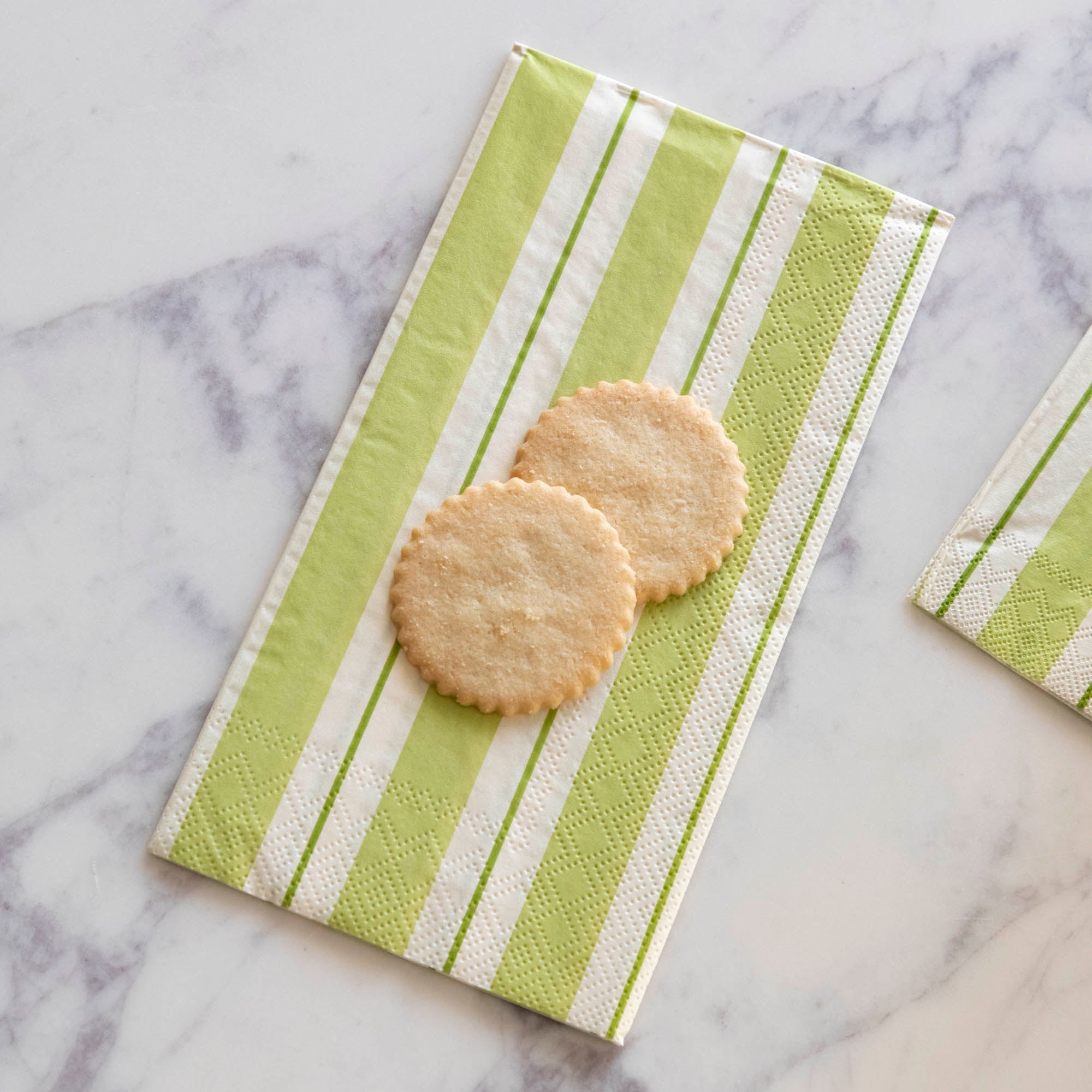 Two sugar cookies sitting on a Green Awning Stripe Guest Napkin on a white table.