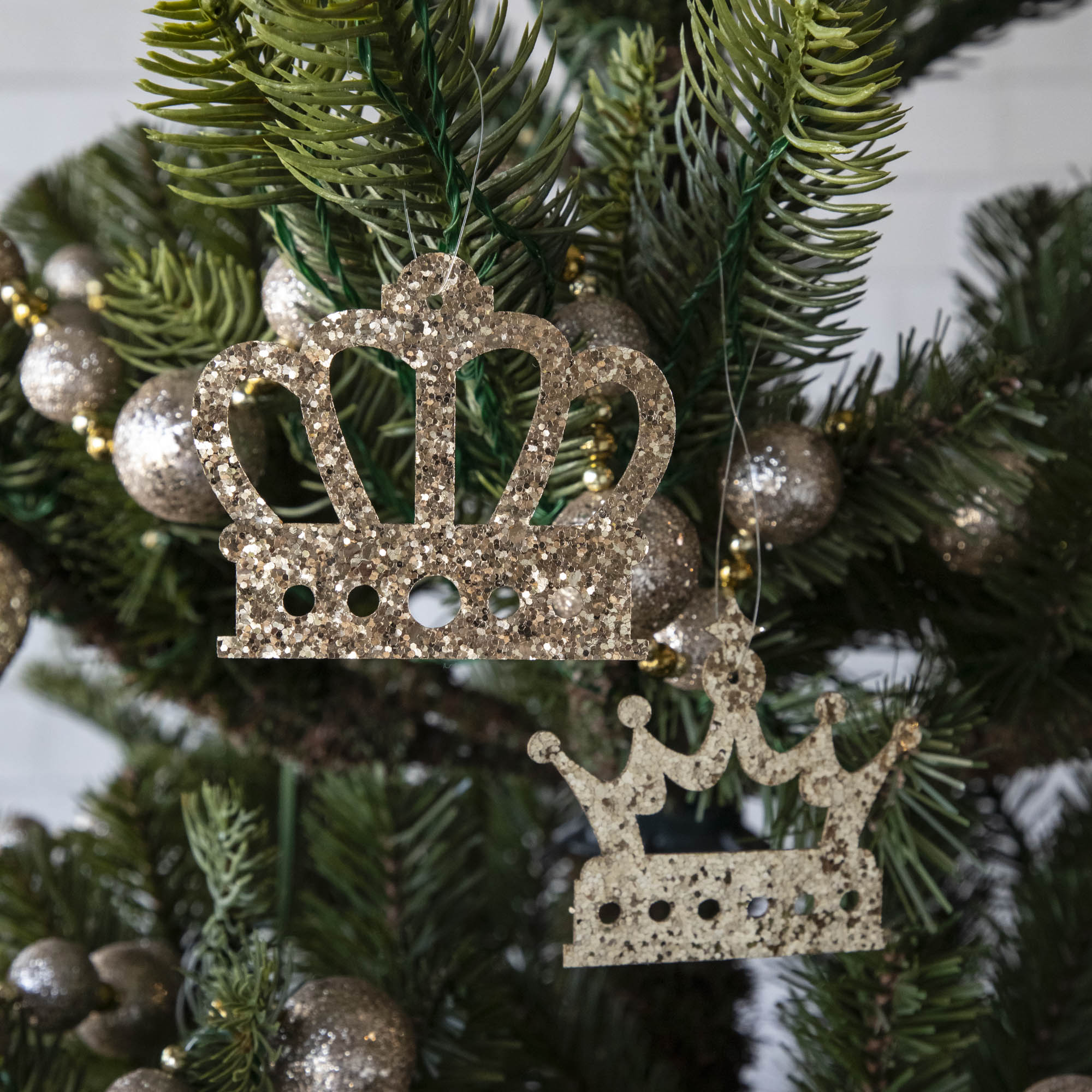 Gold glitter crown-shaped ornaments hanging on a Christmas tree.