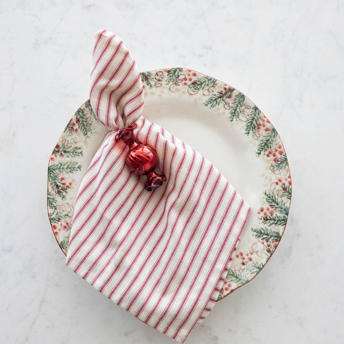 Red Round Glass Candy Shaped Ornament tied to a red stripe napkin on top of a holiday plate