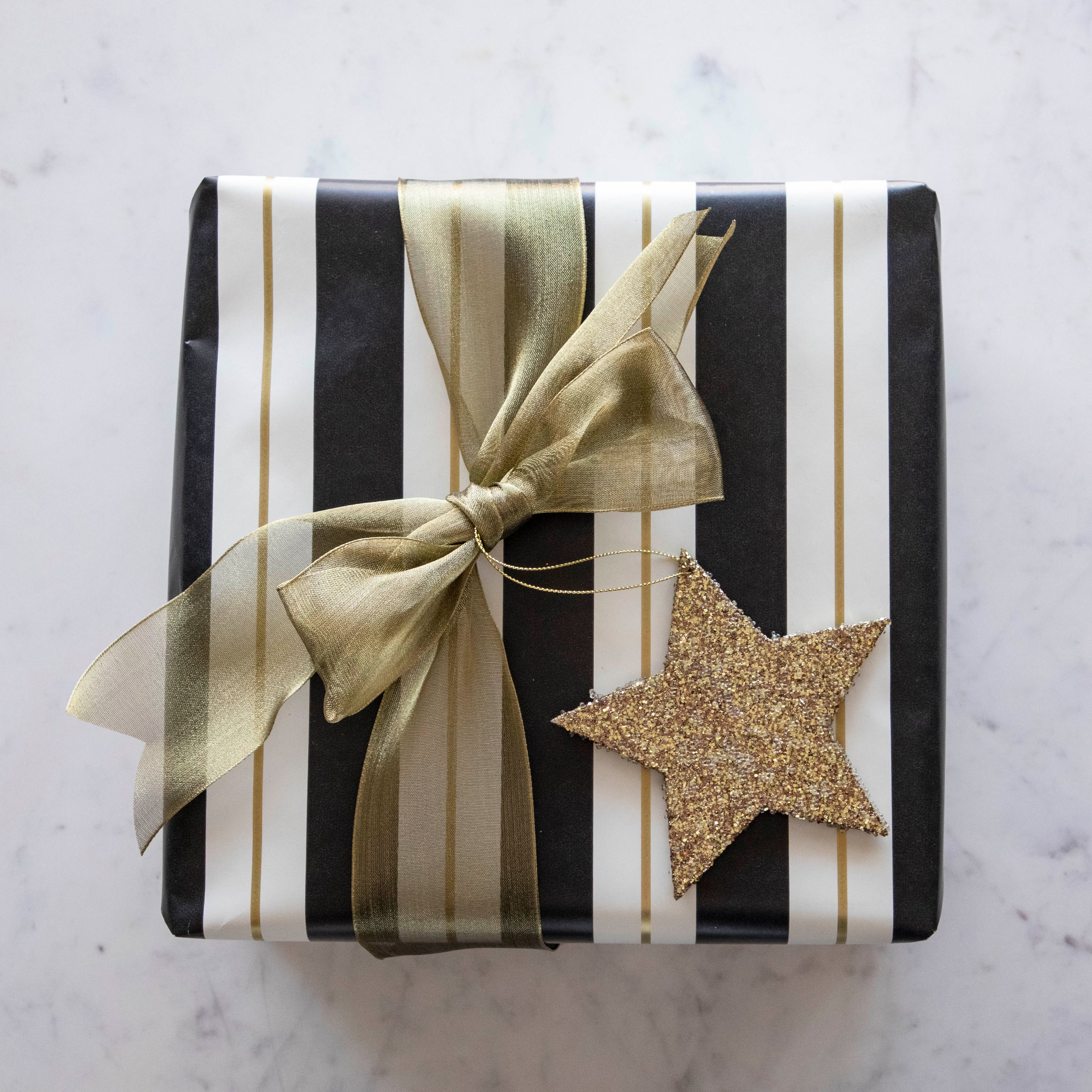 A present wrapped in the Black & Gold Awning Stripe Runner by Hester & Cook, tied with a gold ribbon and star ornament.