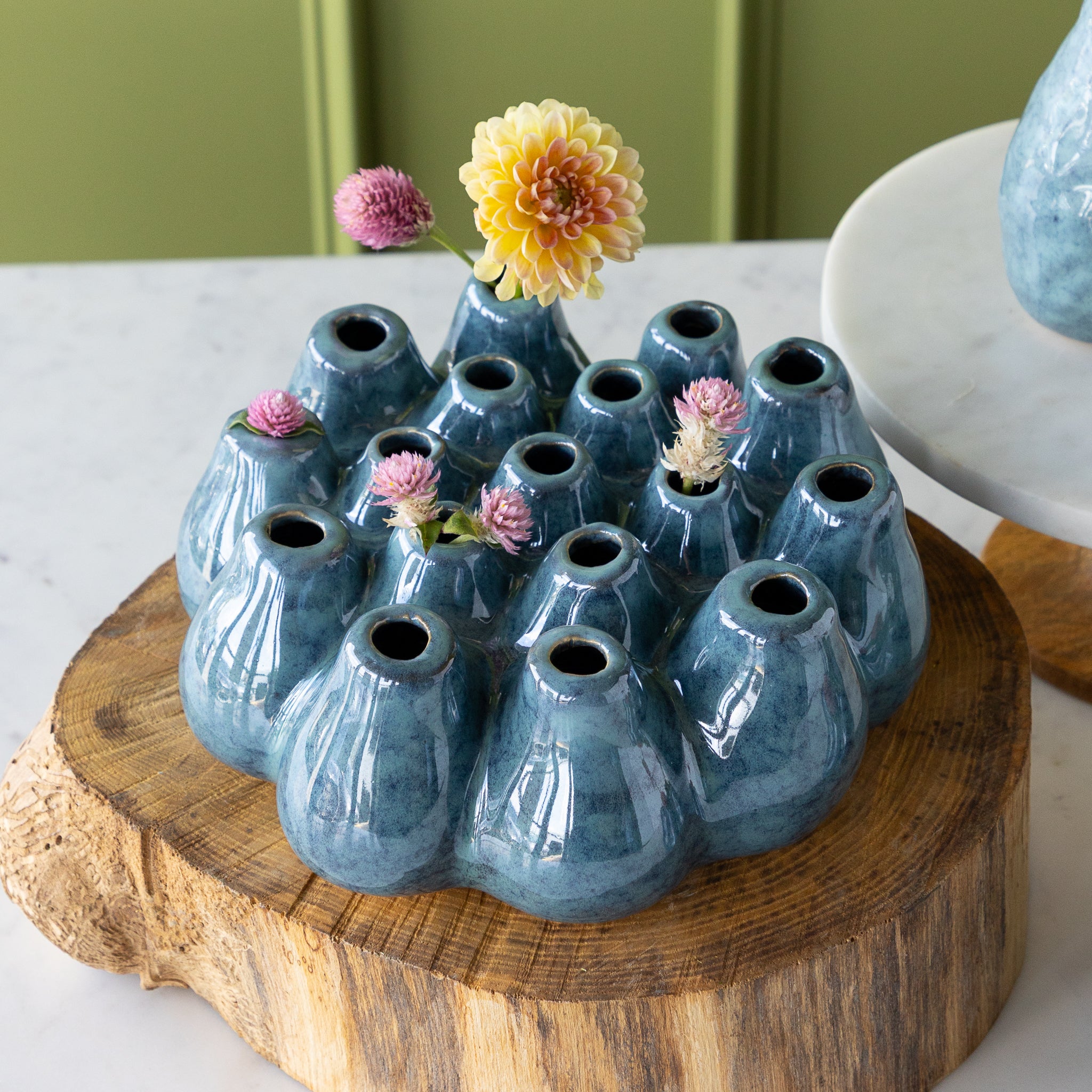A blue ceramic vase with flowers on a wooden stand.