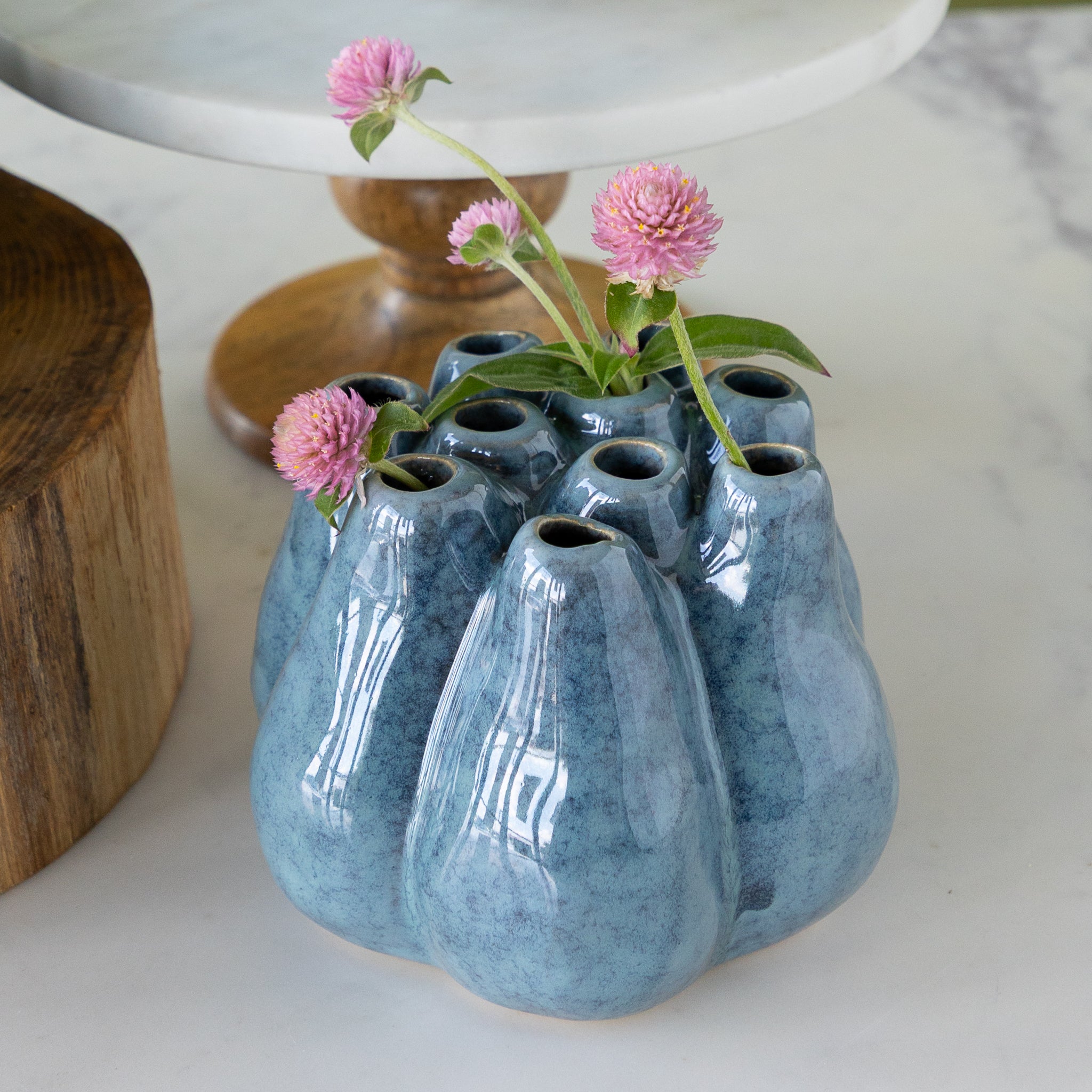 Blue ceramic vase with multiple small holes holding pink flowers on a white surface.
