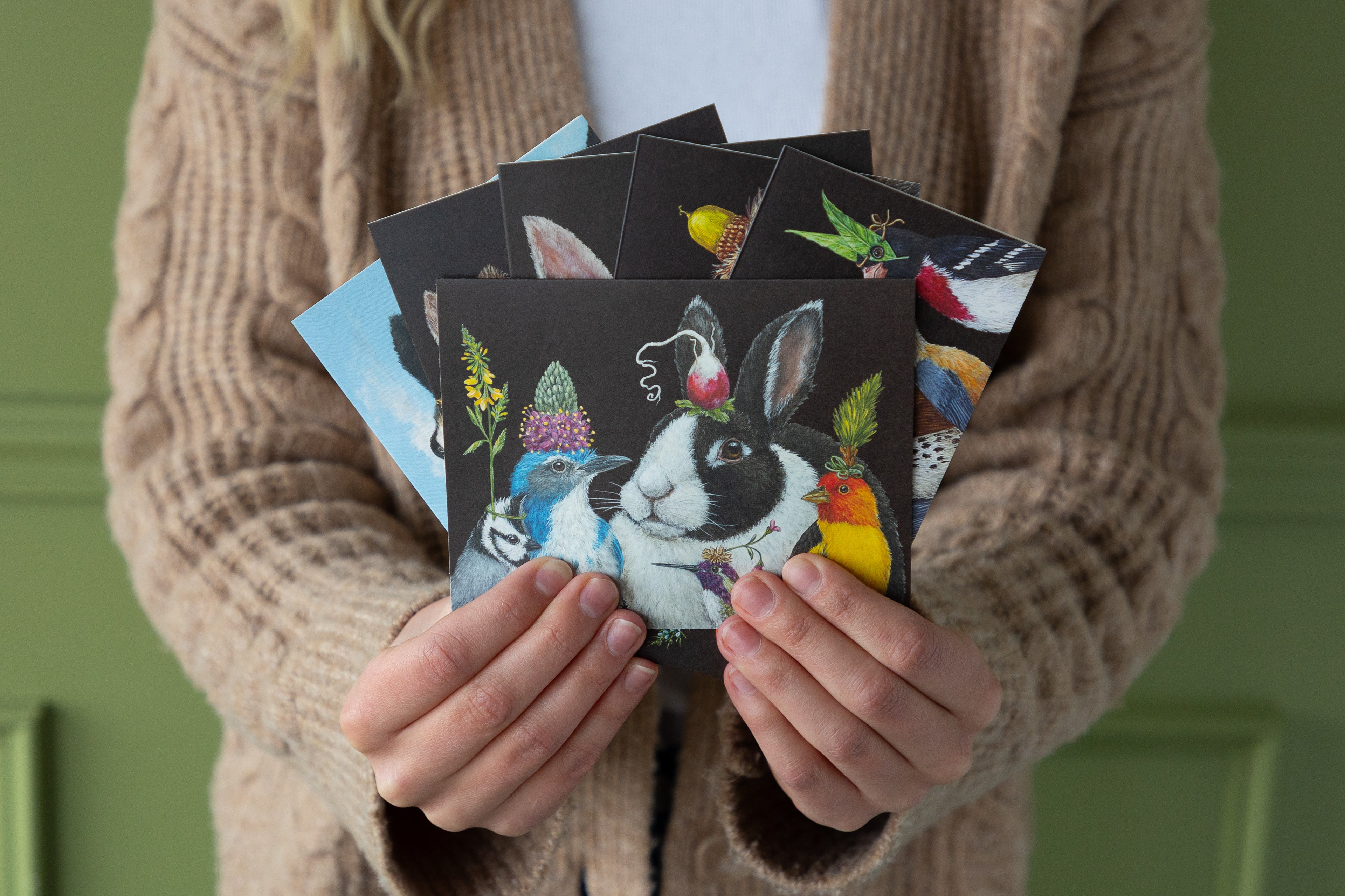Person holding a collection of postcards with animal illustrations against a green background.