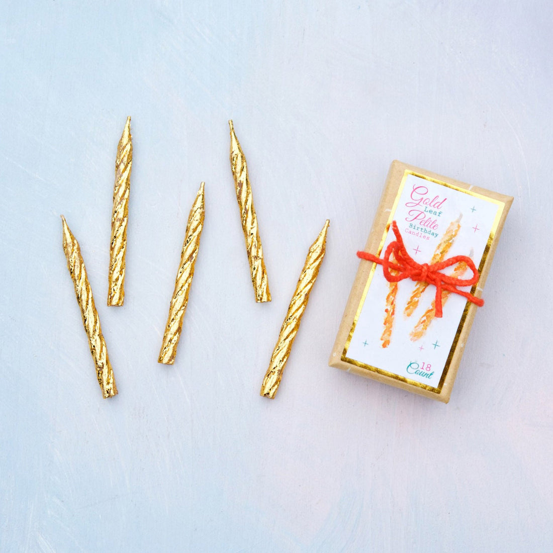 A set of Glitterville Gold Petite Party Candles, Boxed Set of 18 for celebration and a gift box on a table.
