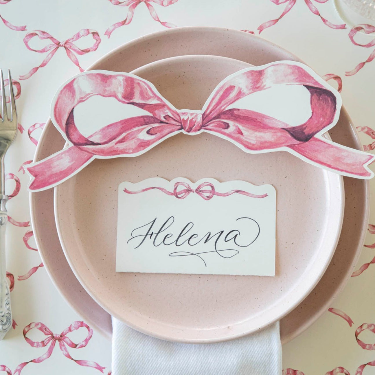 An elegant place setting featuring a Pink Bow Table Accent resting on the plate with a name card.