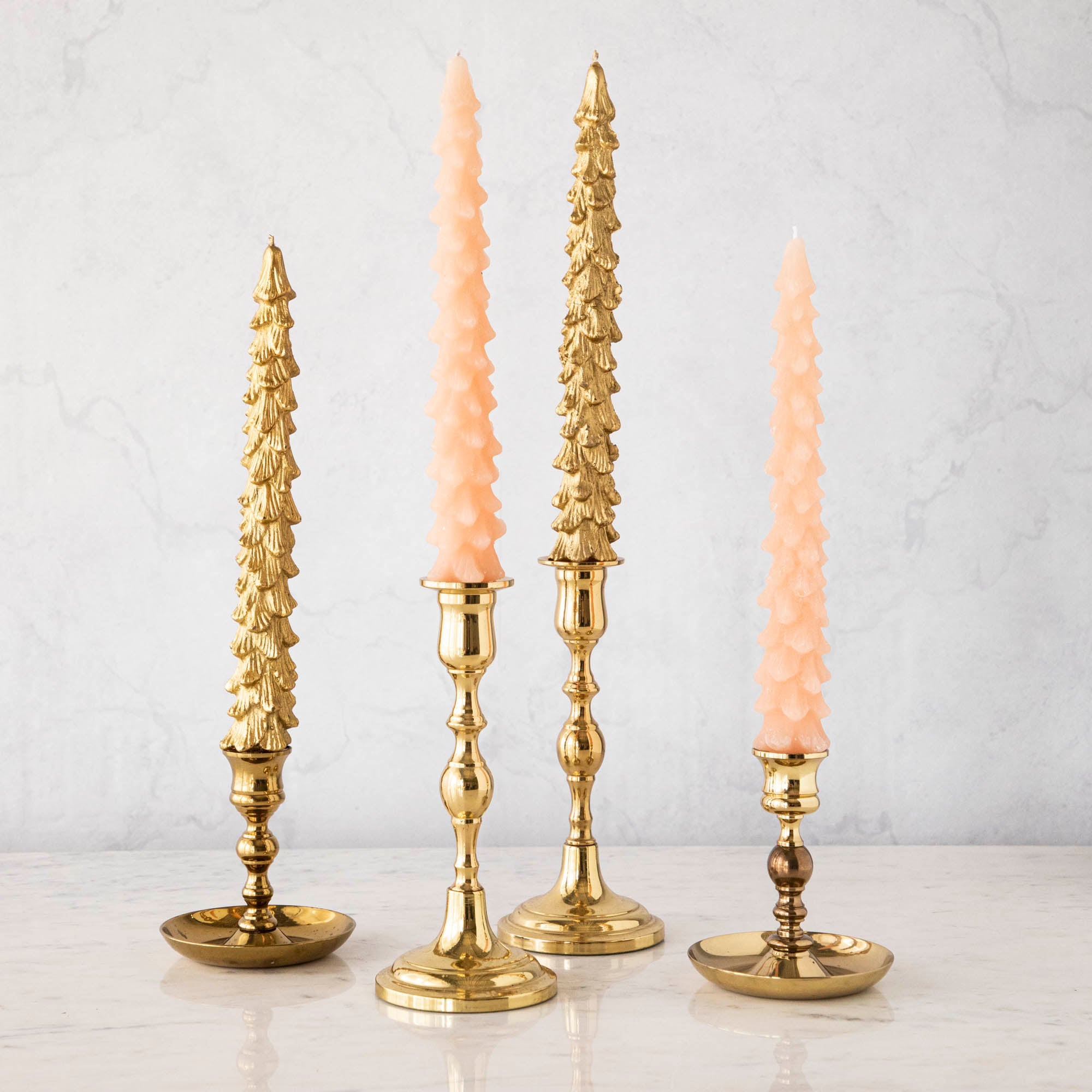 A set of two pink unscented tree-shaped taper candles, with one candle longer than the other, displayed on a surface with a decorative, antique-style gold candle holder.