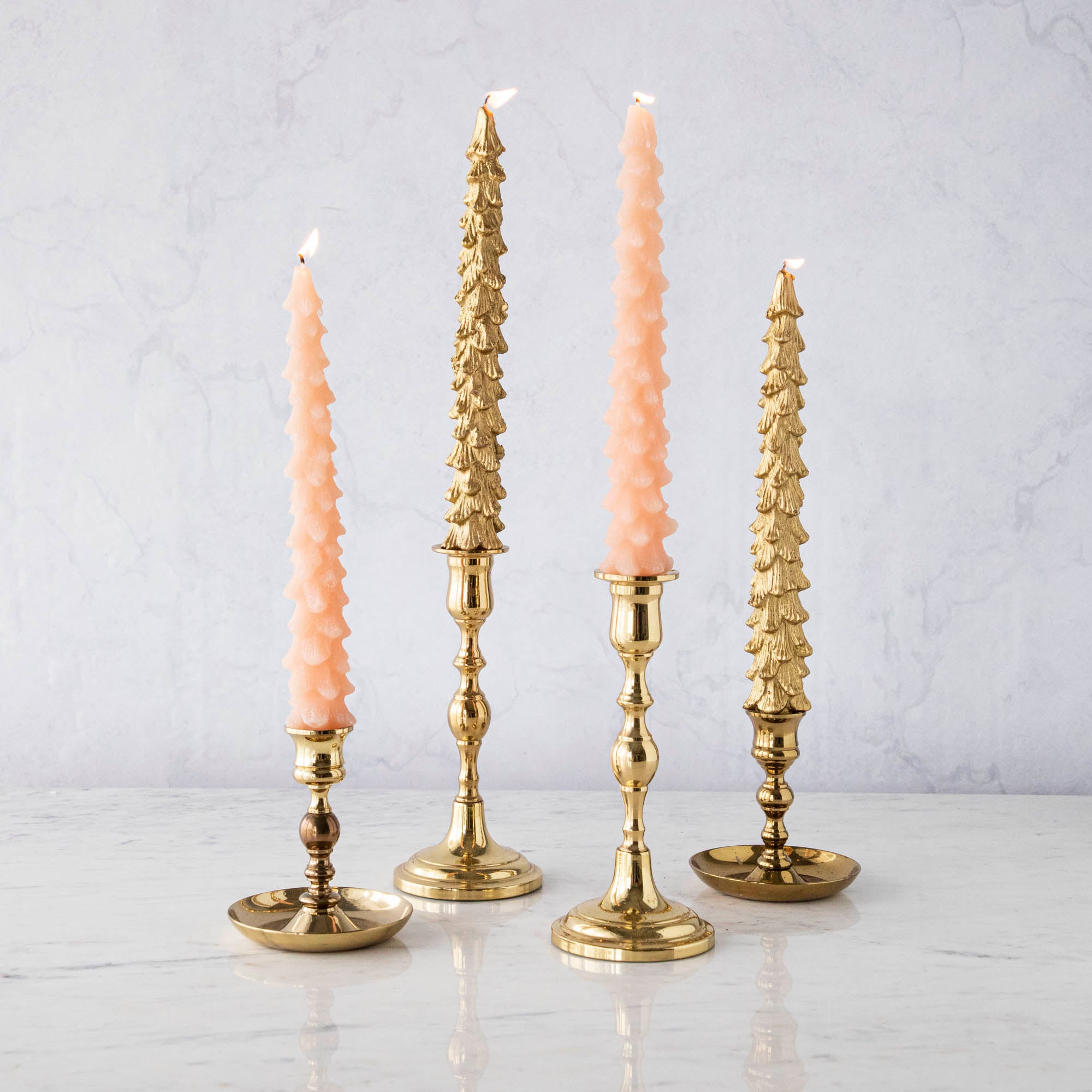 A set of two pink unscented tree-shaped taper candles, with one candle longer than the other, displayed on a surface with a decorative, antique-style gold candle holder.