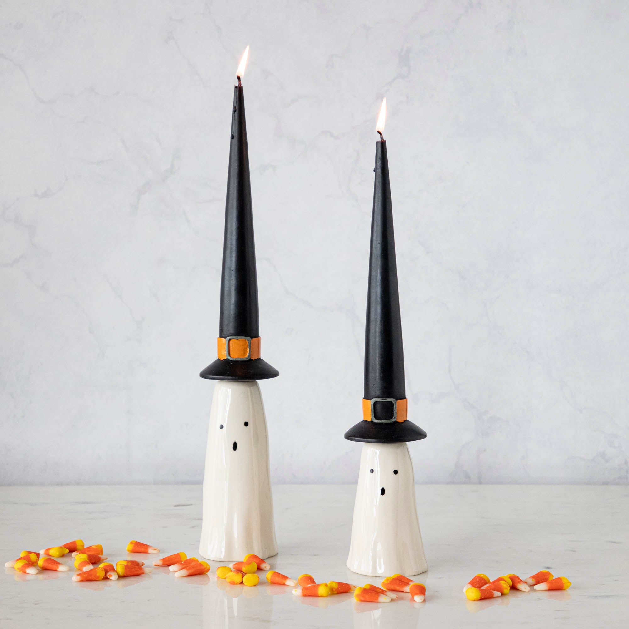 Two Phantom Candleholders from Accent Decor with witch hat candles, on a table surrounded by candy corn. them.