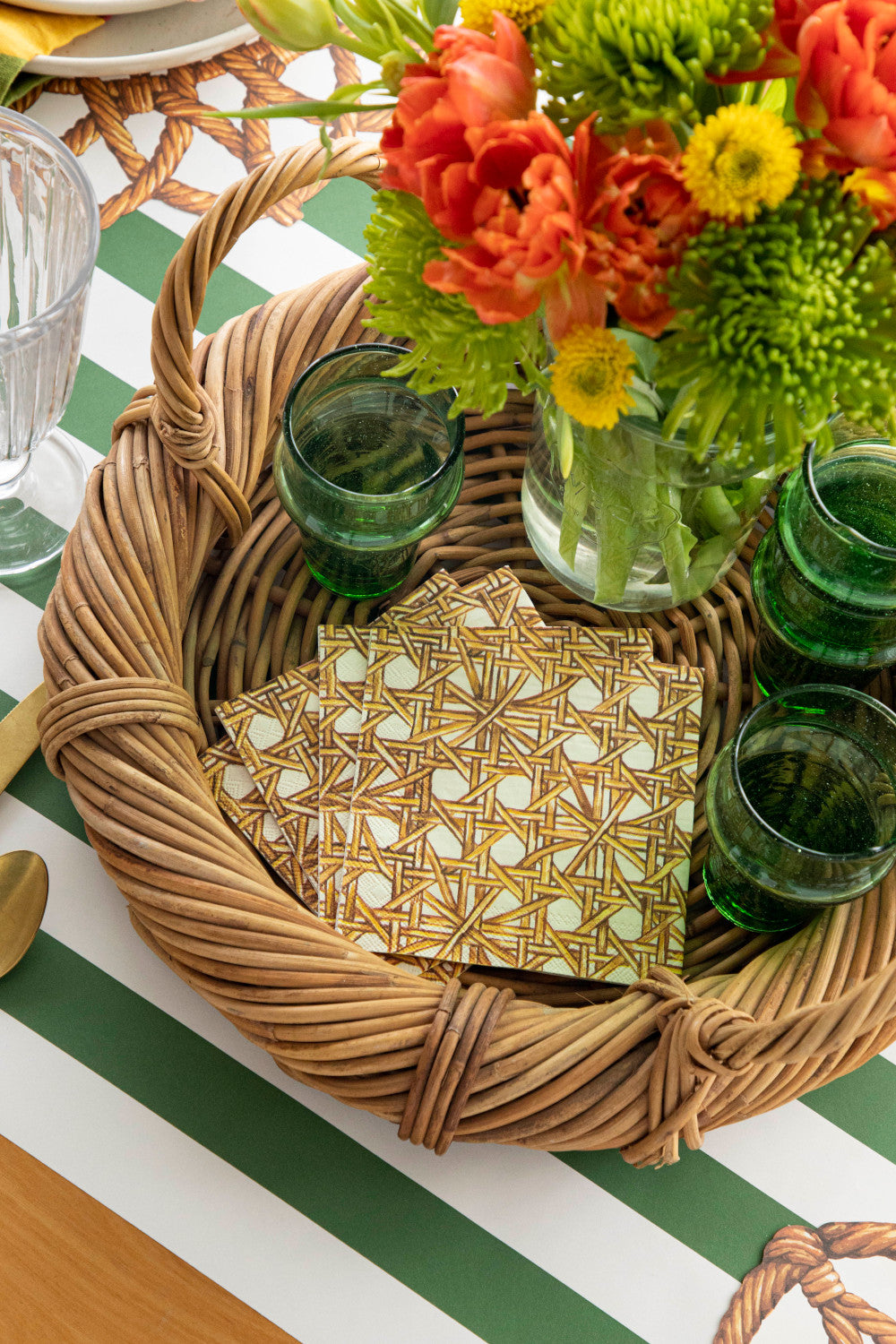 A stack of Rattan Weave Cocktail Napkins on a beverage tray with glasses and a vase of flowers.