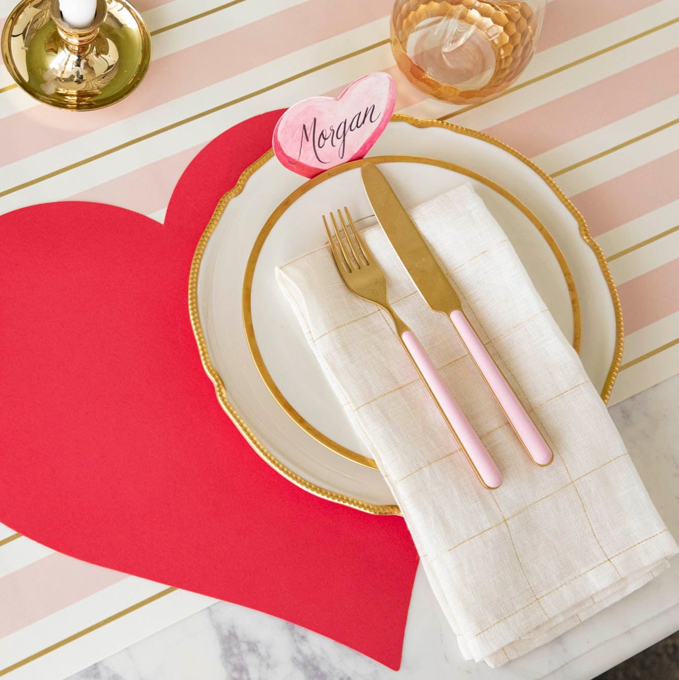 An elegant table setting with the Conversation Heart Place card with "Morgan" written on it, resting on a dinner plate that sits on the Die-cut Red Heart Placemat.