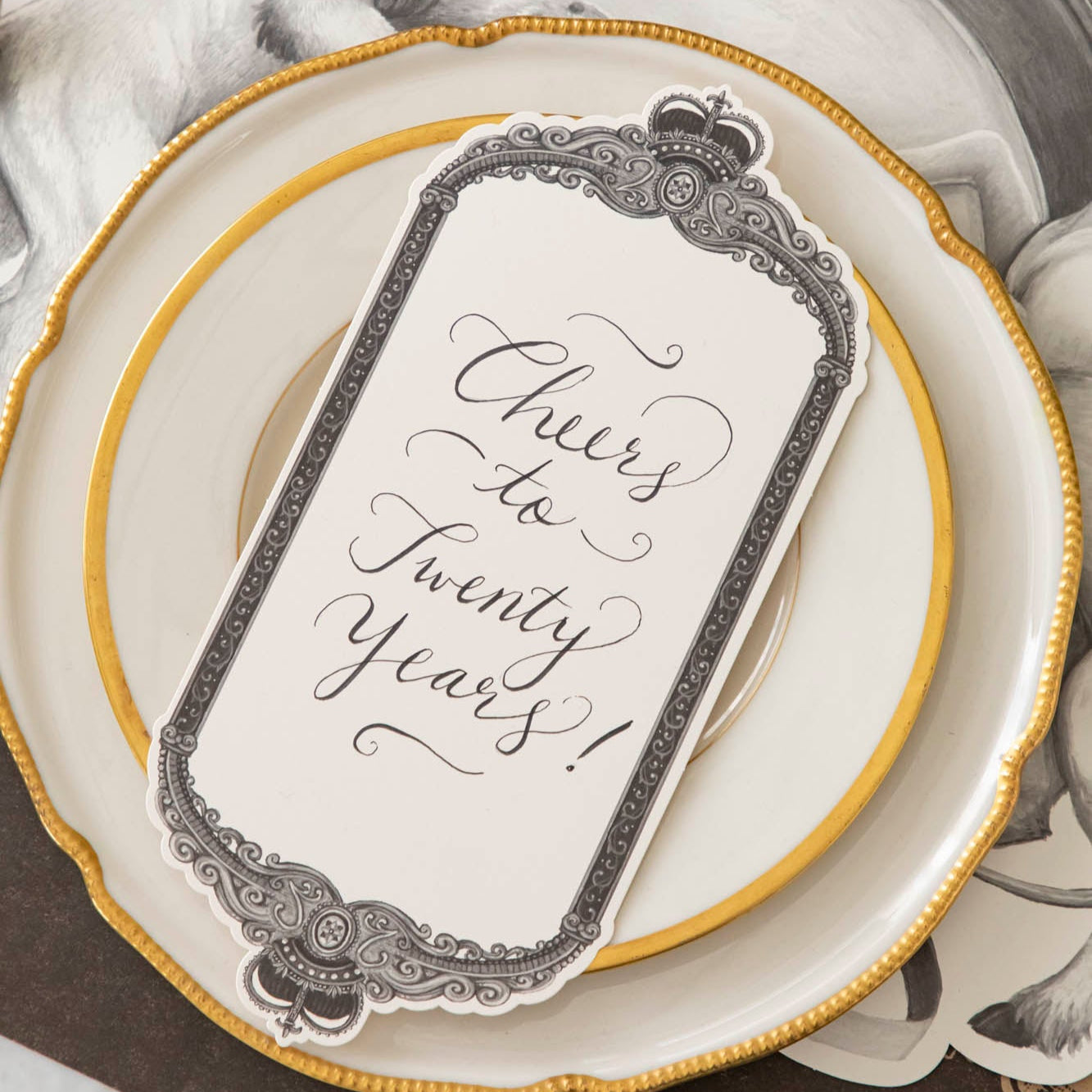 Regal Frame Table Card with "Cheers to Twenty Years!" written on it, resting on dinner plates.