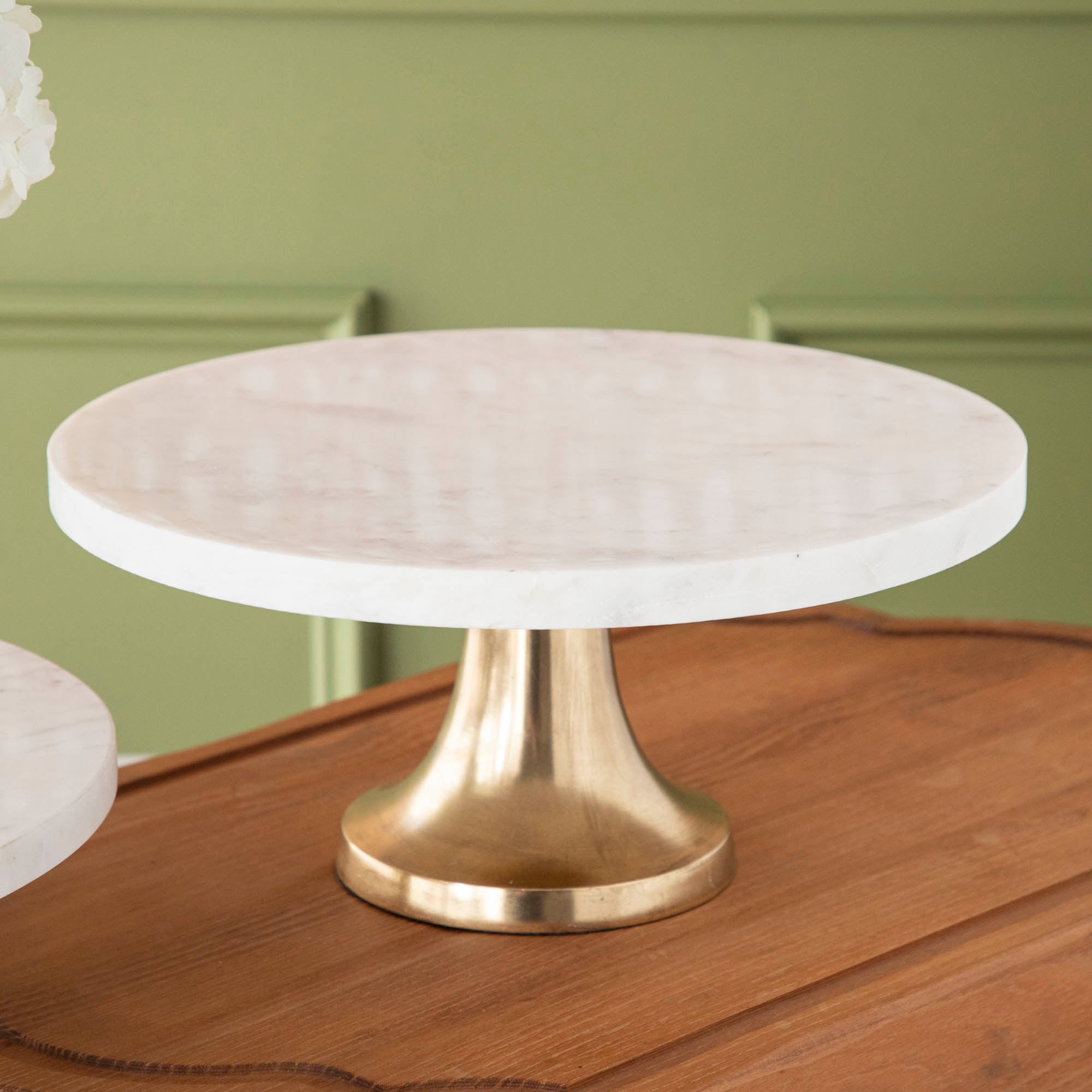 A bouquet of white hydrangeas in a white vase on a Bidk Home Marble Cake Plate with Antique Brass Base with decorative tables and a textured background.