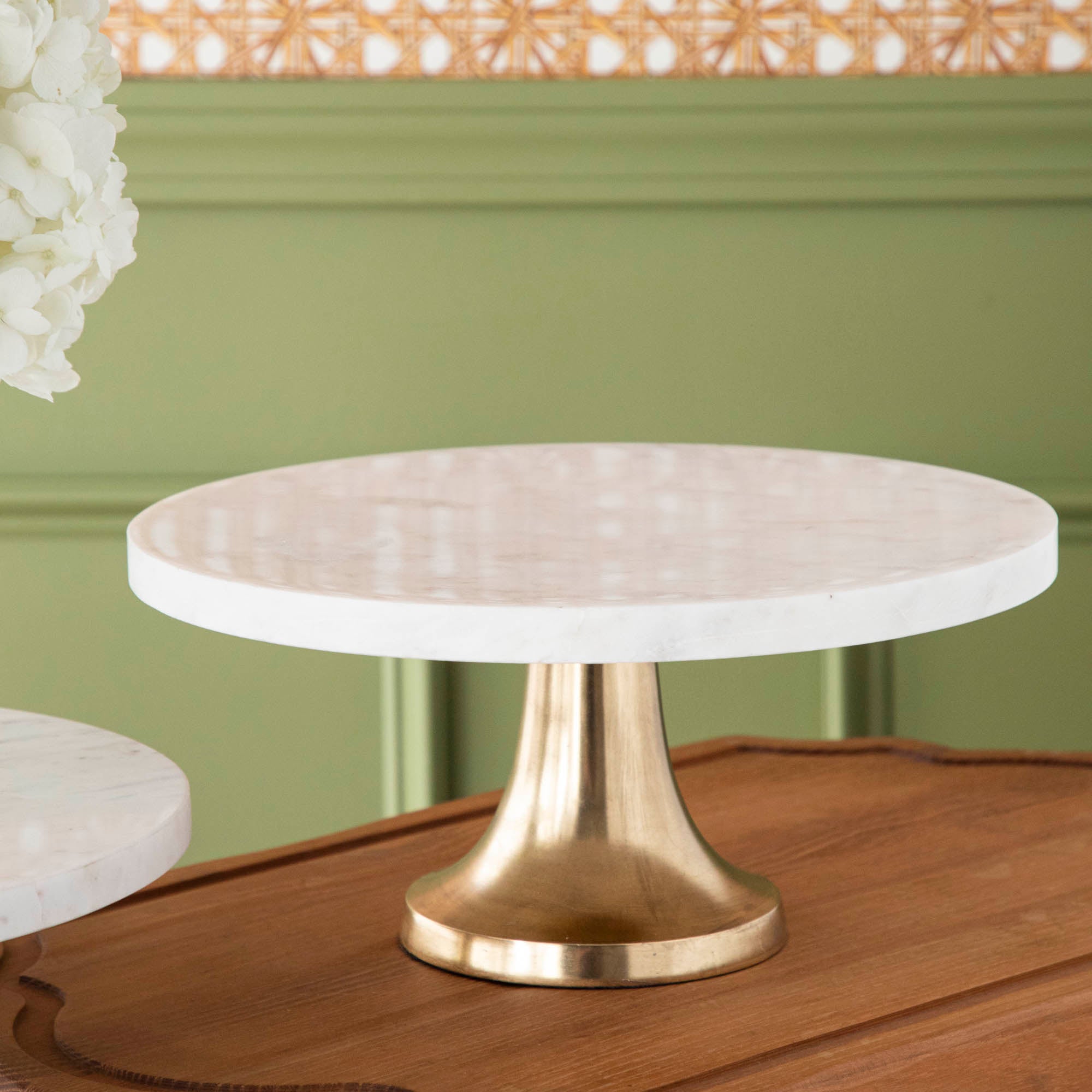 A bouquet of white hydrangeas in a white vase on a Bidk Home Marble Cake Plate with Antique Brass Base with decorative tables and a textured background.
