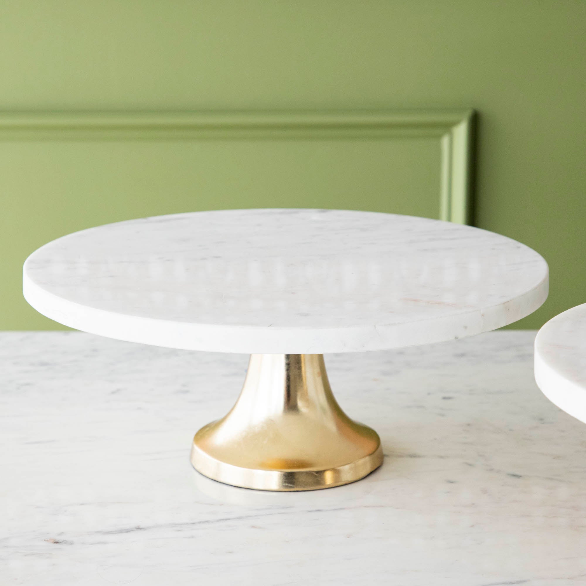 A bouquet of white hydrangeas in a white vase on a Bidk Home Marble Cake Plate with Antique Brass Base with decorative tables and a textured background.