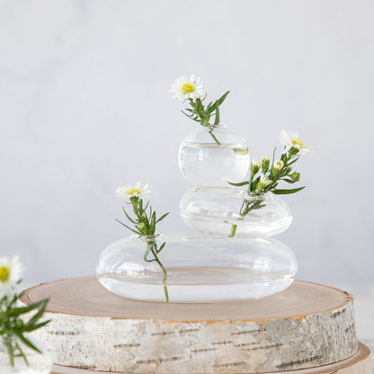 A balanced arrangement of glass spheres with water and white flowers in a Chive Hudson Rockpile Vase on a wooden slab.