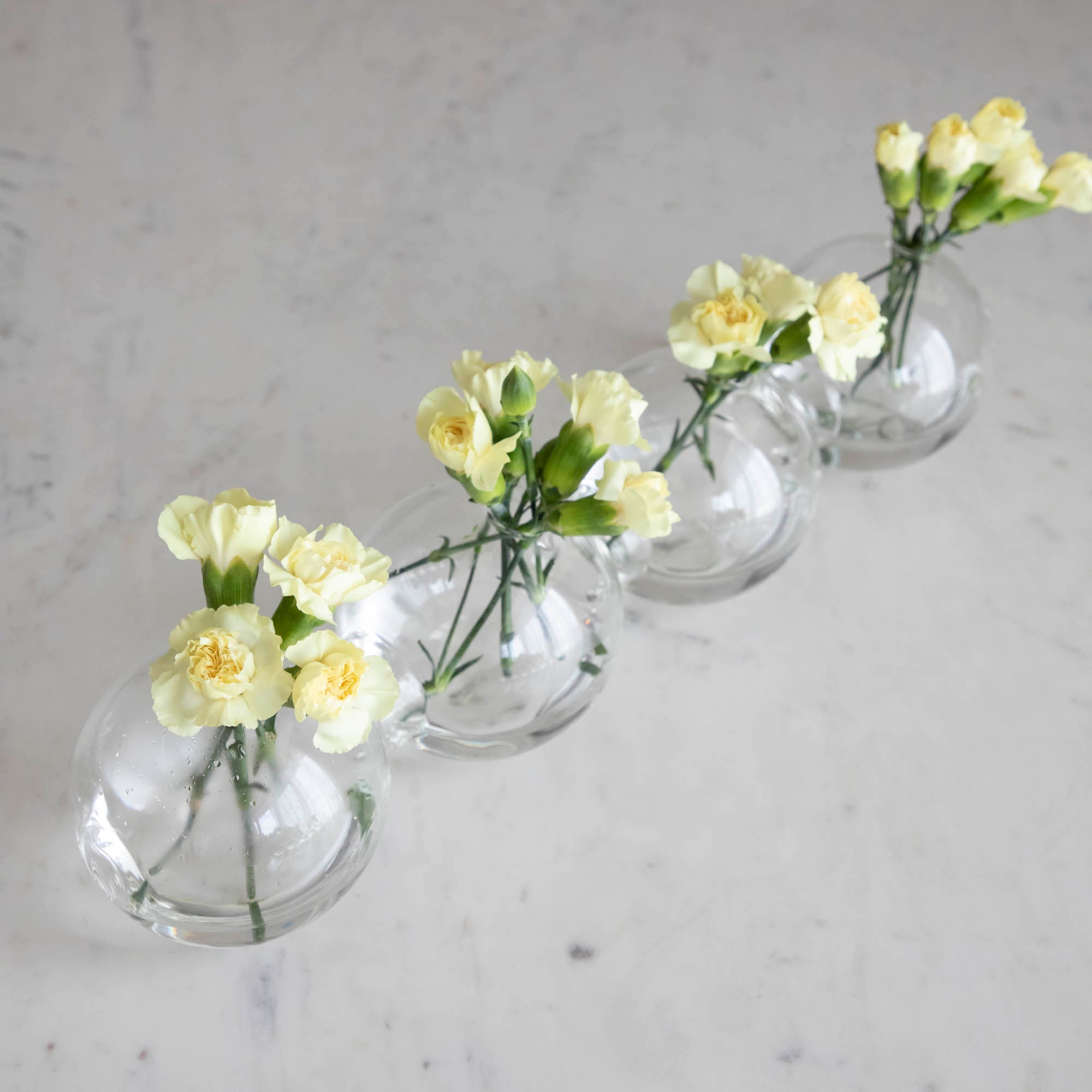 A group of clear glass caterpillar-shaped vases arranged on a surface with water in them, containing yellow flowers.