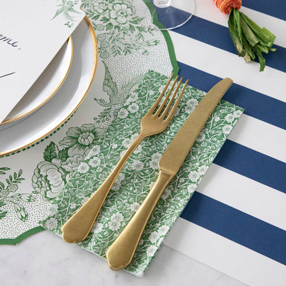 A Green Calico Guest Napkin under gold cutlery in an elegant place setting.