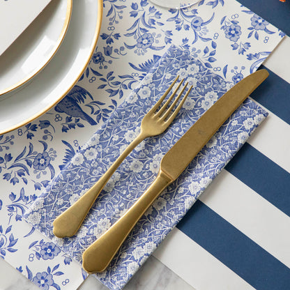 An elegant place setting with a Blue Calico Guest Napkin under a gold fork and knife next to a plate.