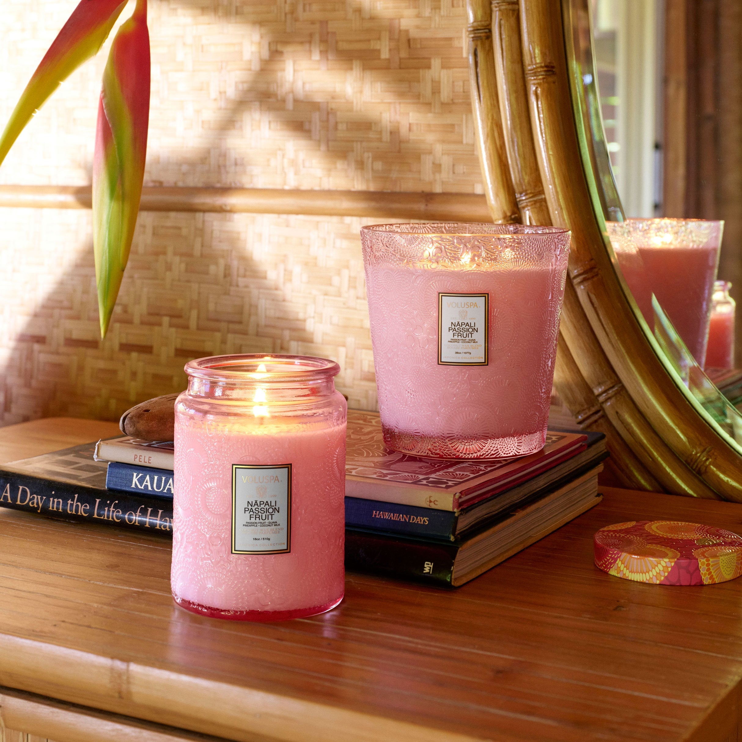Two pink candles on a wooden surface with books and a mirror in the background.