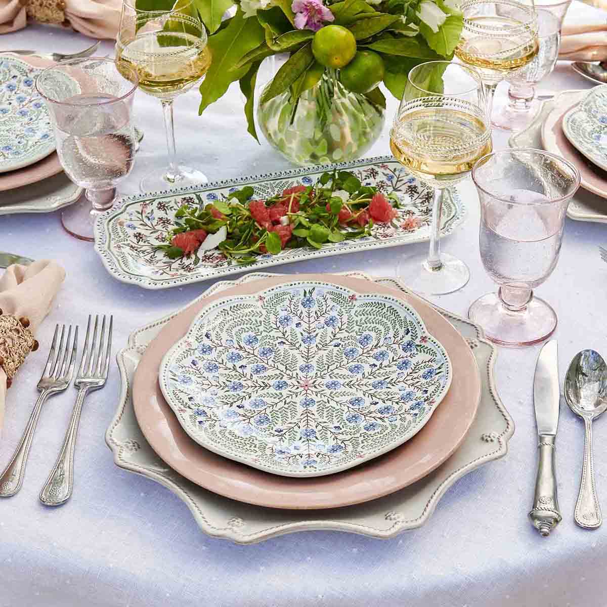 An elegantly set dining table with Juliska Villa Seville dinner plates, silverware, and glasses of wine.