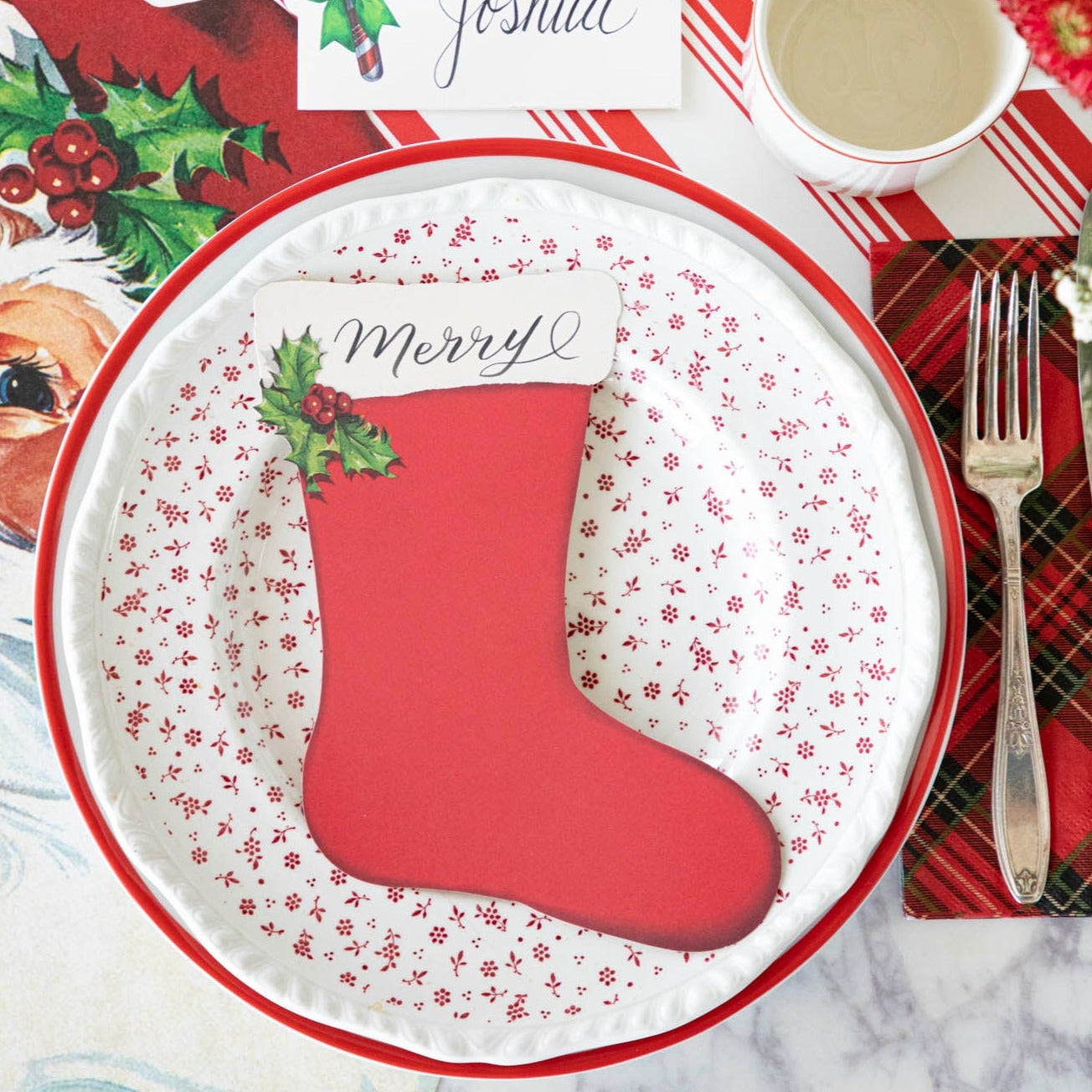 The Stocking Table Accent with "Merry" written on it, resting on a plate, on a Christmas themed table setting.