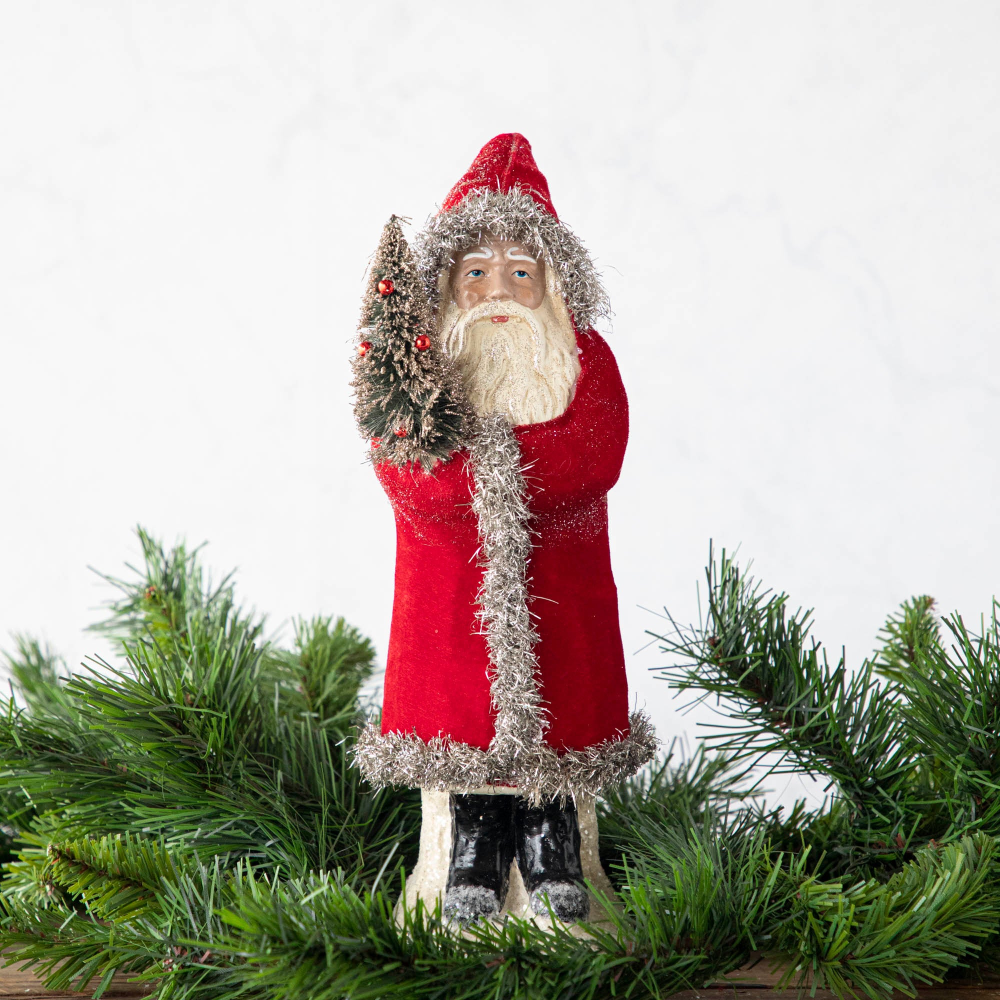A 12" Velvet Belsnickle figurine with a bright red velvet robe adorned with tinsel trimming and glitter, holding a tree.