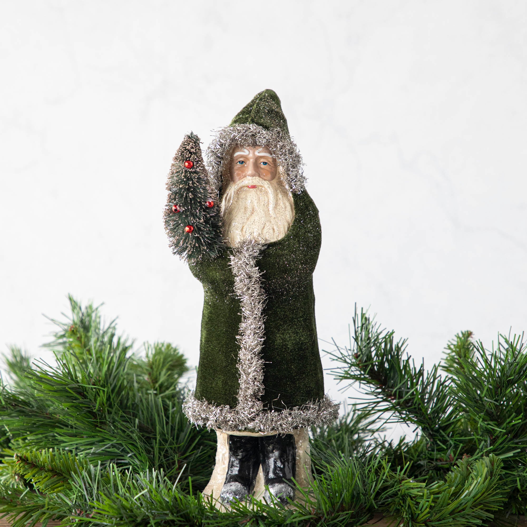 A 12" Velvet Belsnickle figurine with a forest green velvet robe adorned with tinsel trimming and glitter, holding a tree.