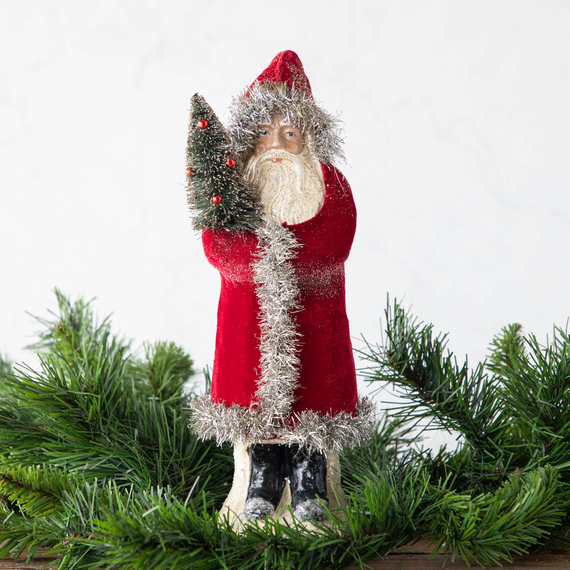 A 12" Velvet Belsnickle figurine with a dark red velvet robe adorned with tinsel trimming and glitter, holding a tree.