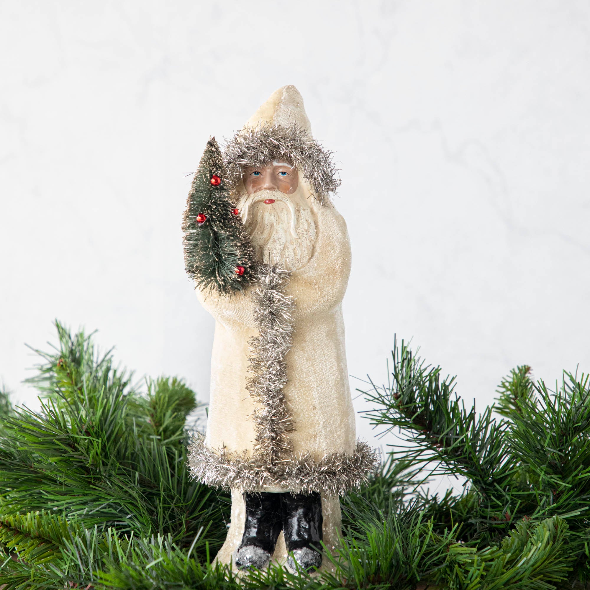 A 12" Velvet Belsnickle figurine with a white velvet robe adorned with tinsel trimming and glitter, holding a tree.