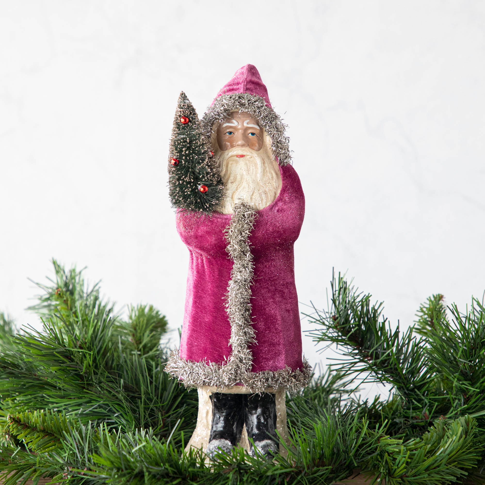 A 12" Velvet Belsnickle figurine with a pink velvet robe adorned with tinsel trimming and glitter, holding a tree.