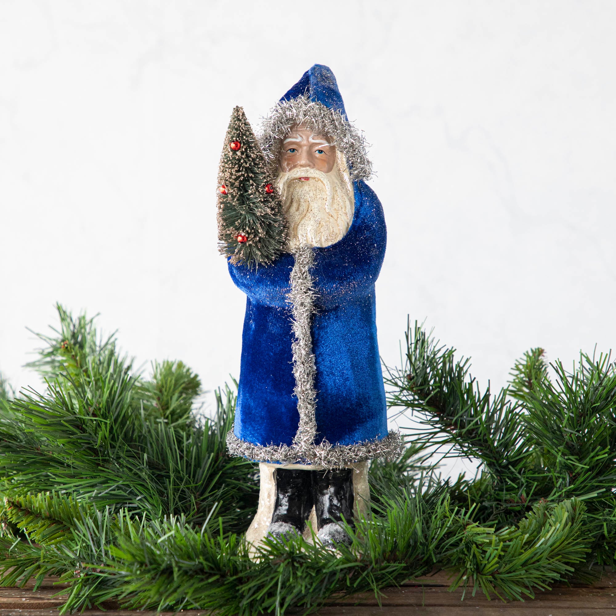 A 12" Velvet Belsnickle figurine with a navy velvet robe adorned with tinsel trimming and glitter, holding a tree.