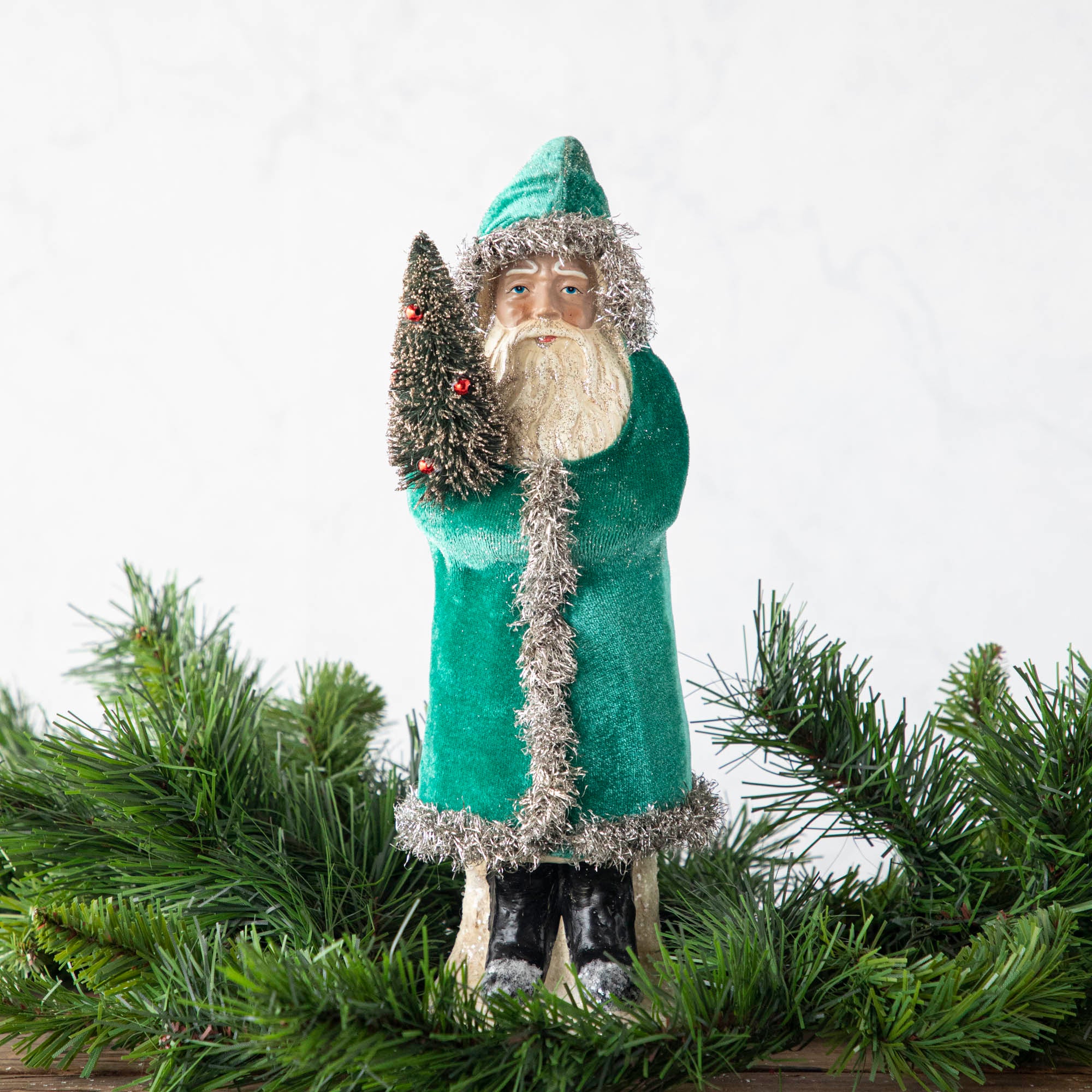 A 12" Velvet Belsnickle figurine with a teal velvet robe adorned with tinsel trimming and glitter, holding a tree.