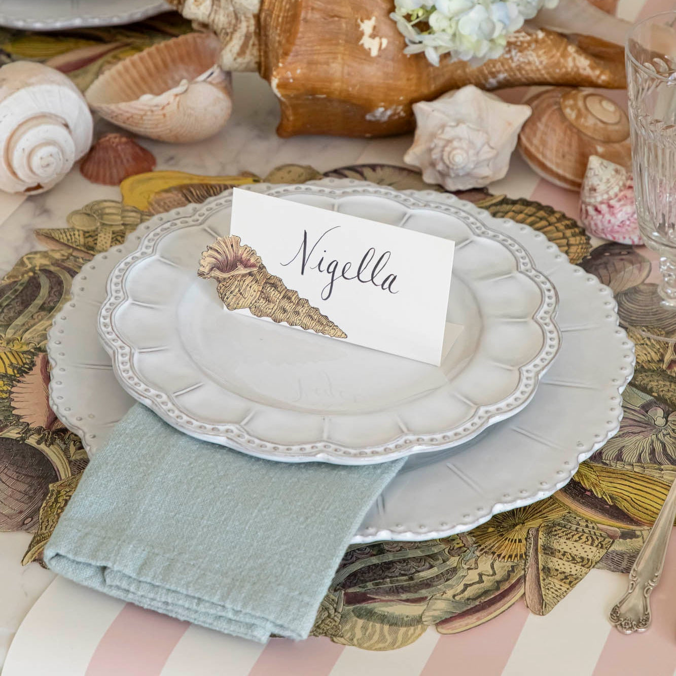 Shell Place Card with "Nigella" written in the white space, on a set of dinner plates on an elegant place setting.