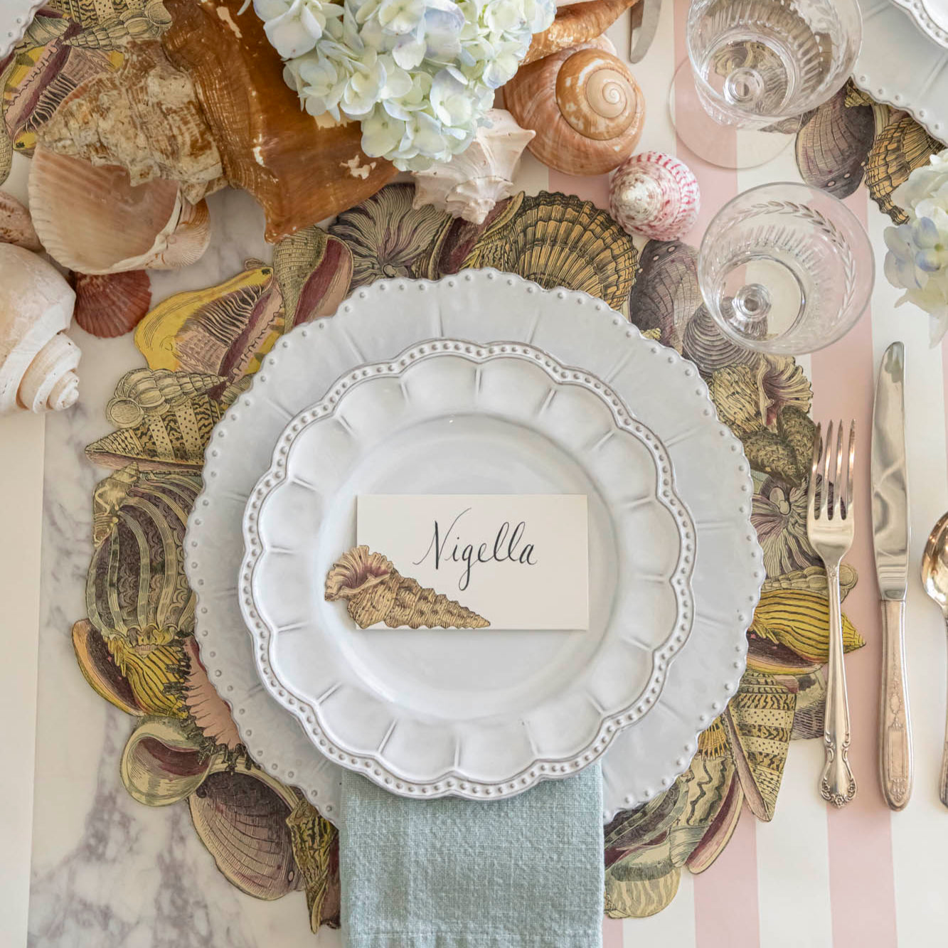 Die-cut Shell Wreath Placemat under a place setting on a shell themed table.